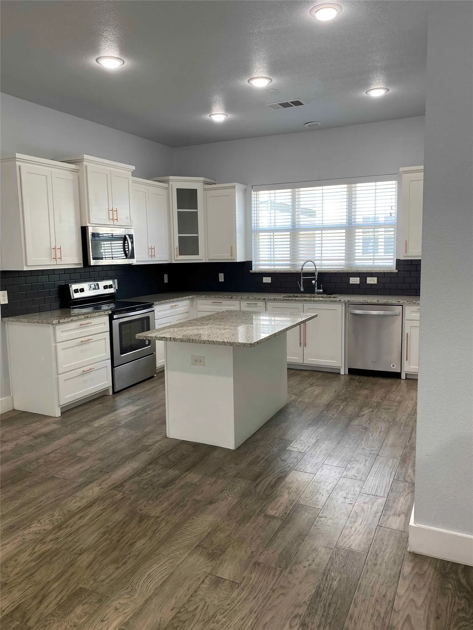 Kitchen with white cabinets, stainless steel appliances, light stone countertops, backsplash, and a kitchen island