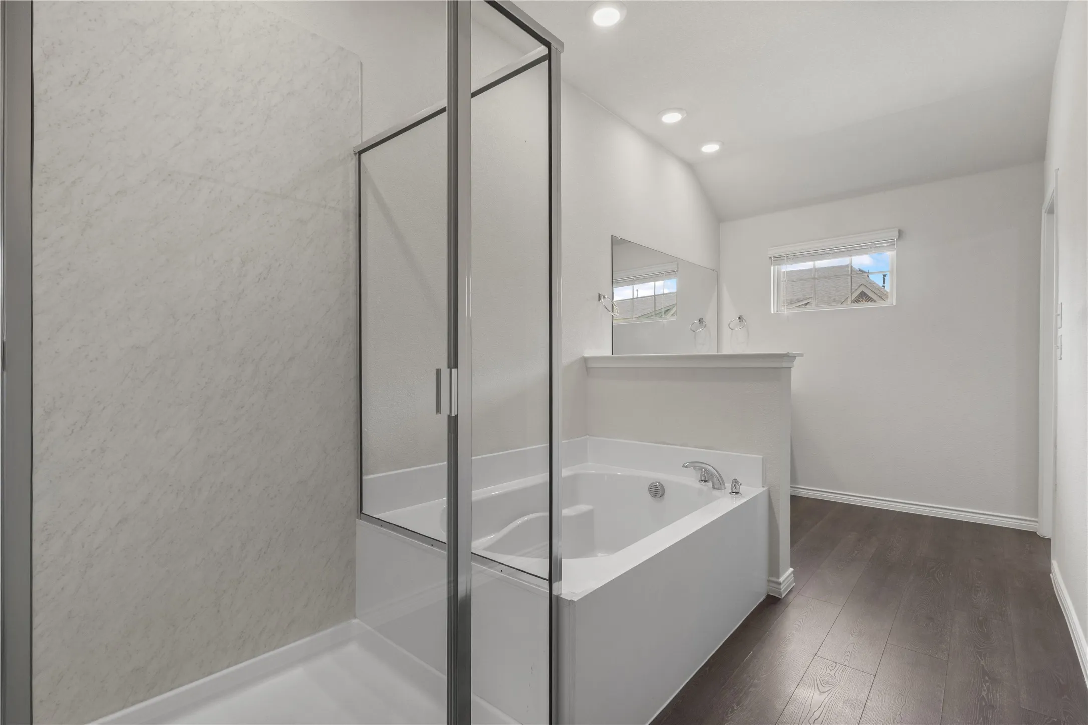 Bathroom featuring a garden tub, lofted ceiling, wood finished floors, a stall shower, and baseboards