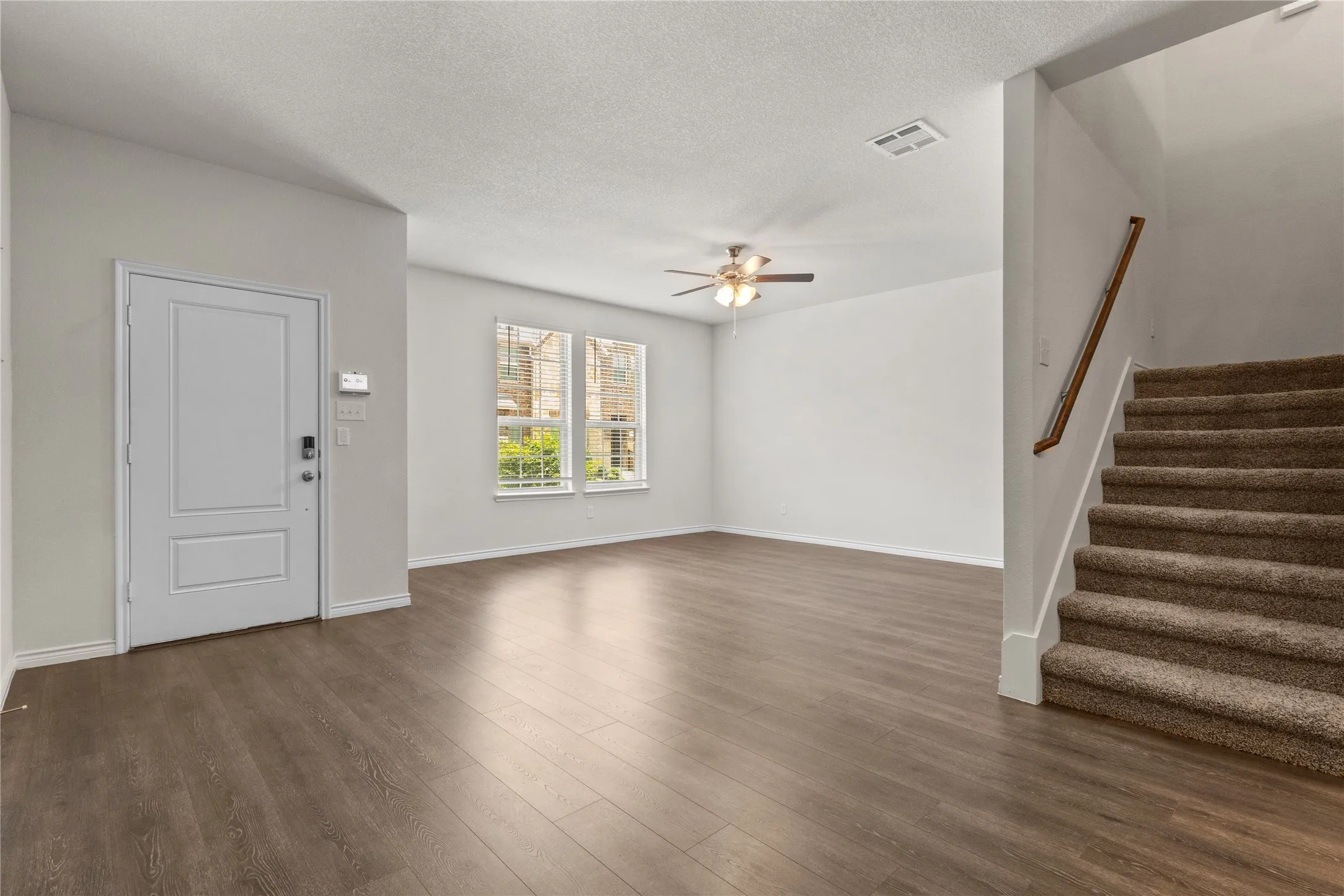 Unfurnished living room with a ceiling fan, stairway, dark wood finished floors, a textured ceiling, and baseboards