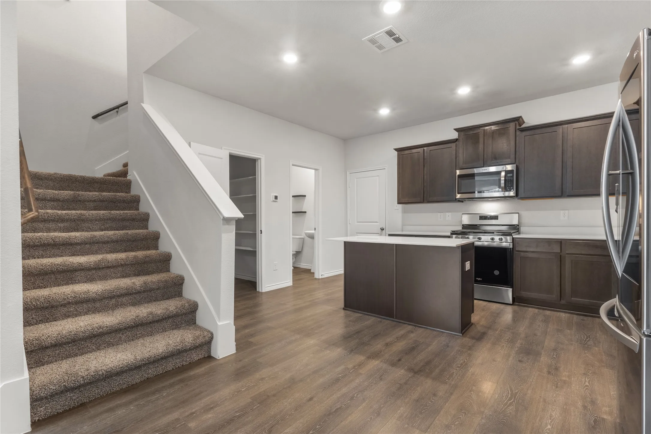 Kitchen featuring appliances with stainless steel finishes, a kitchen island, dark brown cabinets, light countertops, and dark wood-style floors