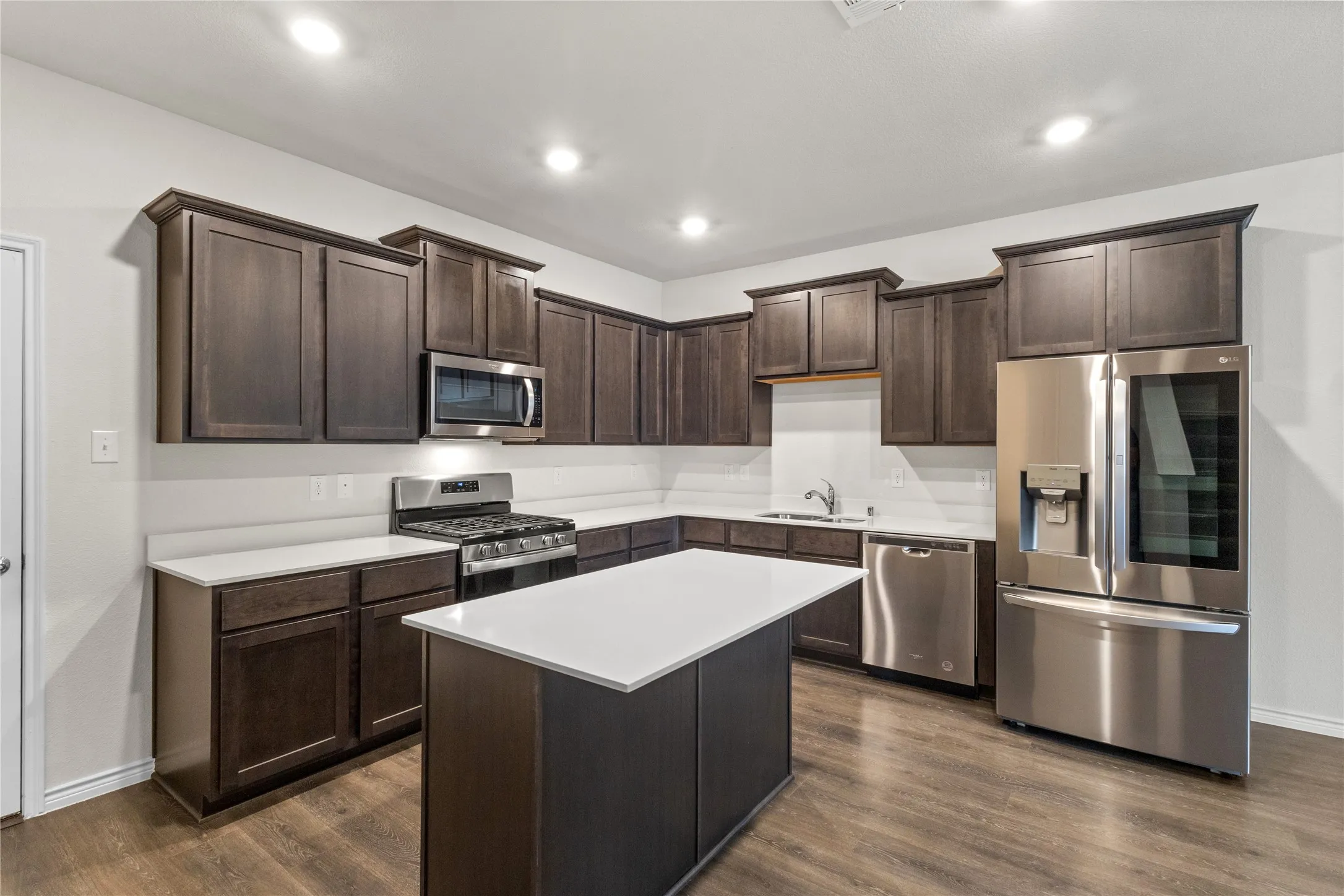 Kitchen with appliances with stainless steel finishes, dark brown cabinets, baseboards, a sink, and light countertops
