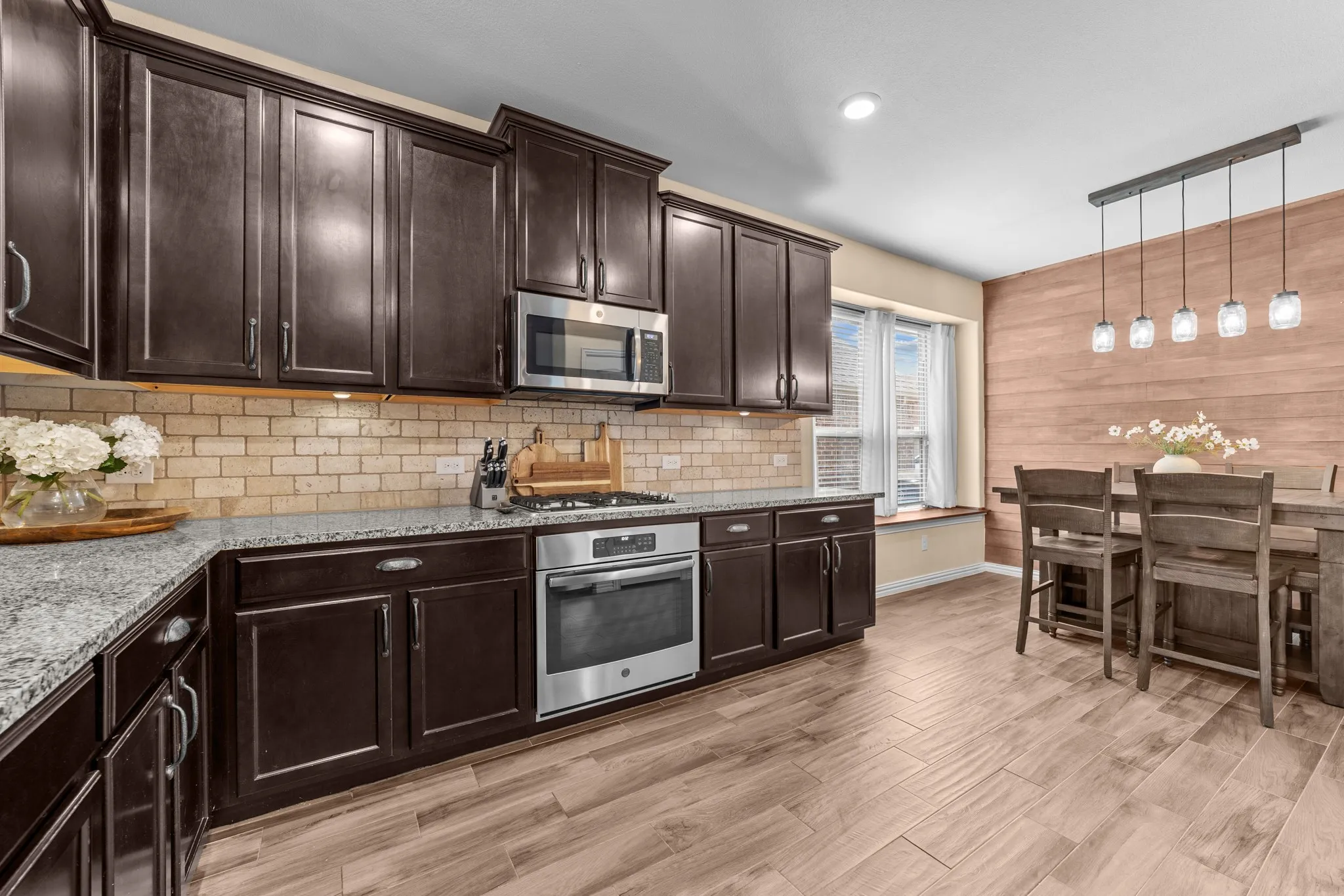 Kitchen featuring dark wood cabinetry, stainless steel appliances, light-toned brick-style backsplash, and stone countertops