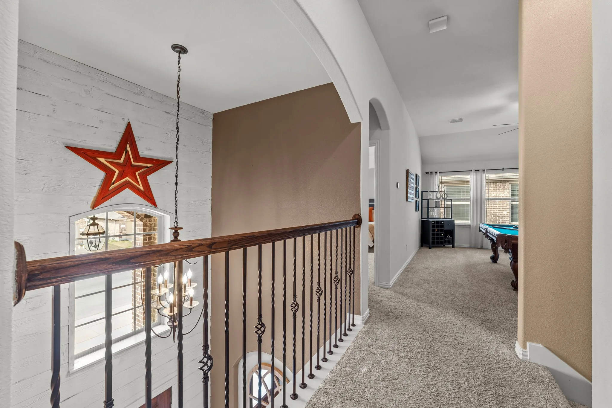 Upper-level hallway featuring white shiplap accent wall, wood-finish railing with metal balusters, pendant lighting, neutral carpet flooring, and access to multiple rooms with arched doorways