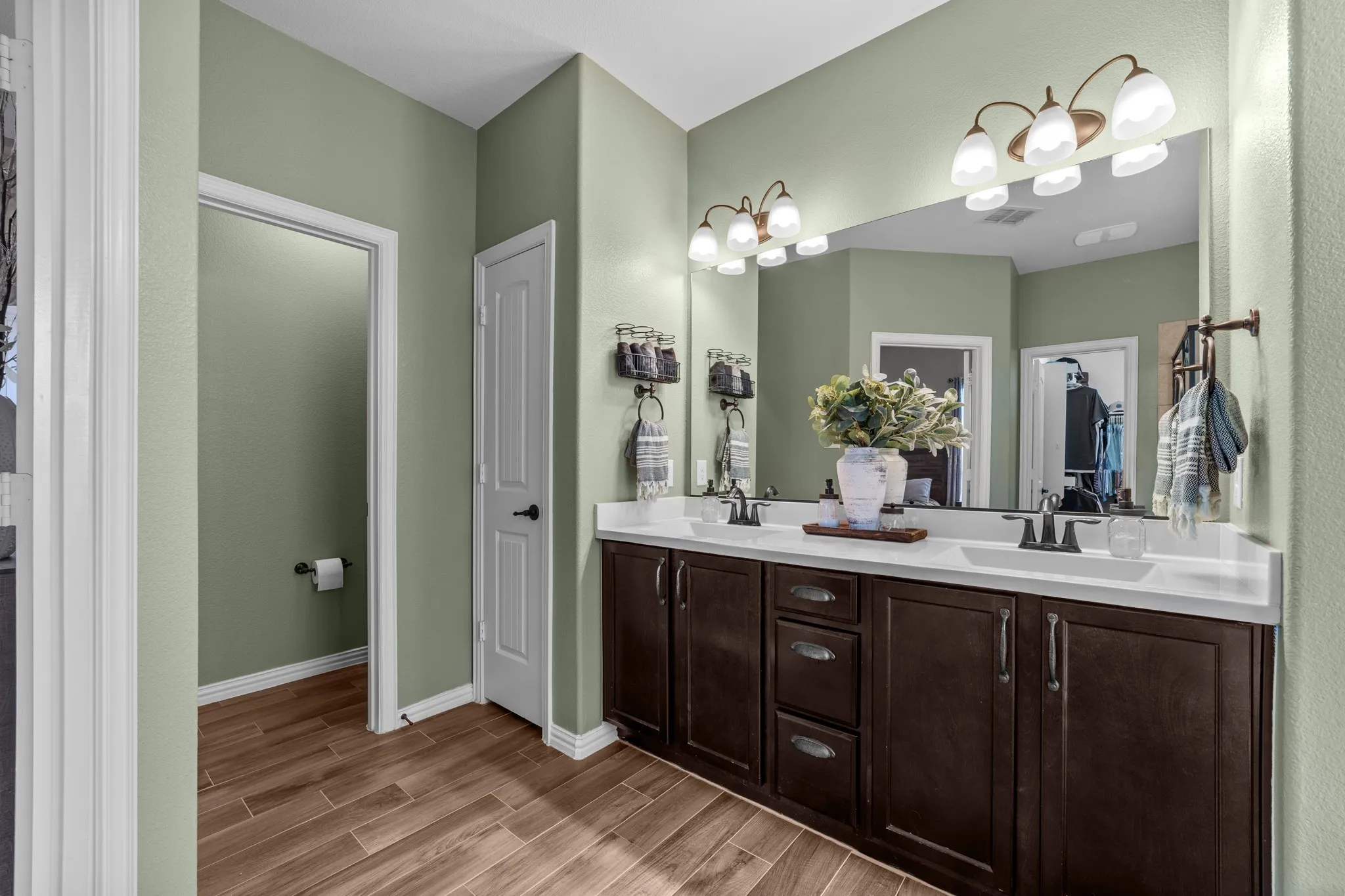 Wood-finish flooring with a dual vanity featuring dark wood cabinetry and white countertops