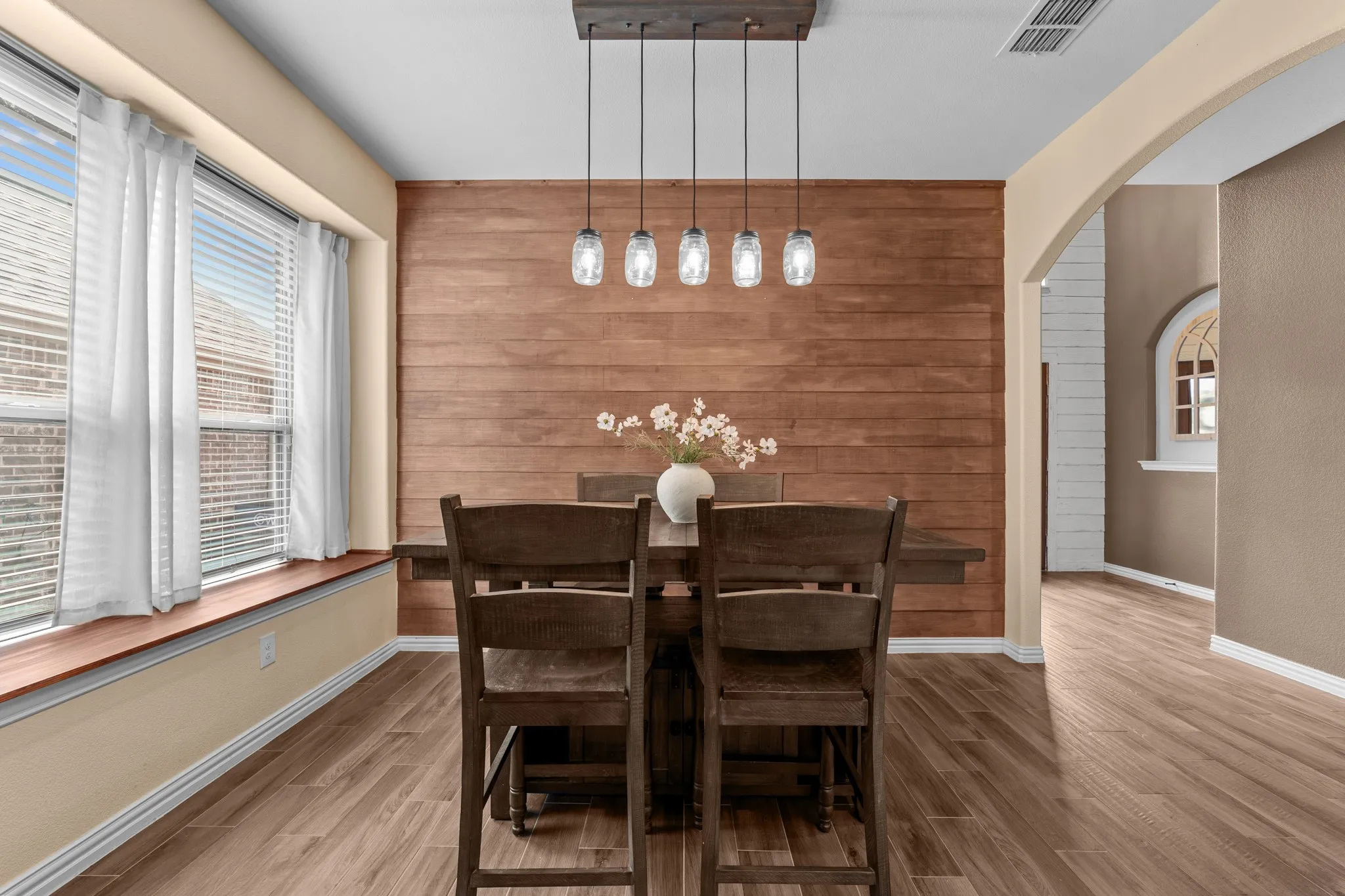 Wood-finish flooring, accent wood panel wall, large window with deep sill, arched entryway, and a five-light linear pendant fixture