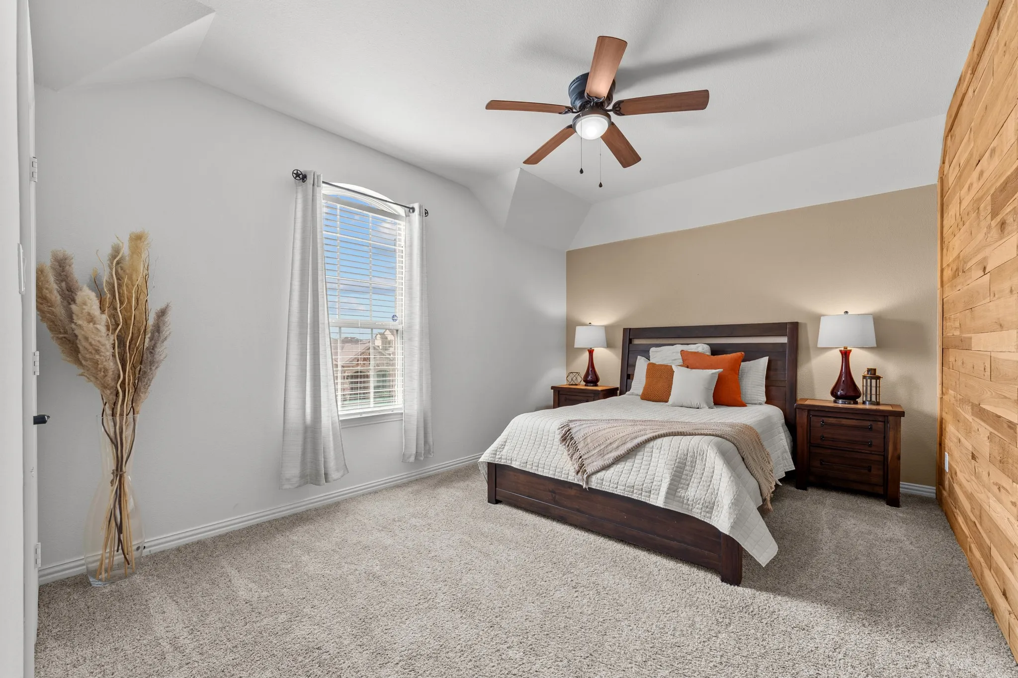 Secondary bedroom suite featuring a wood-frame bed with upholstered headboard, dual wood nightstands with integrated lighting, carpeted flooring, ceiling fan with wood-finish blades, and abundant natural light from a multi-pane window with white trim and plantation shutters