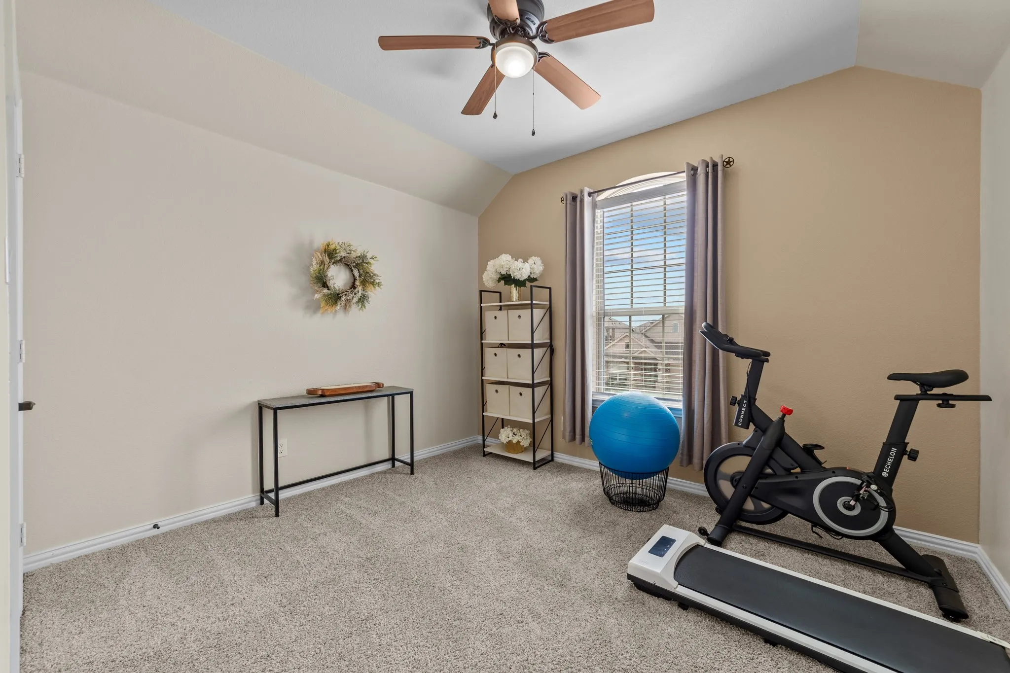 Neutral-toned carpeting, window with blinds, vaulted ceiling, and ceiling fan with integrated lighting
