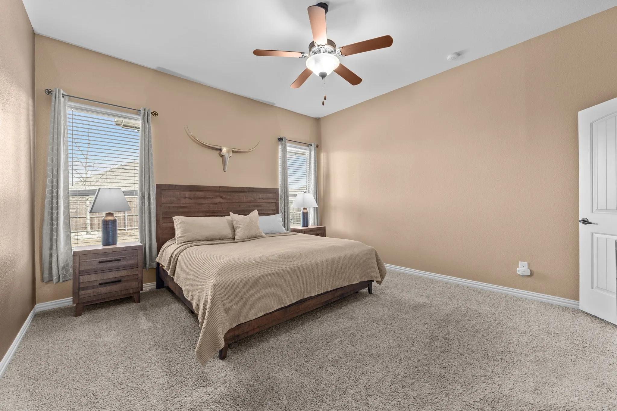 Carpeted room featuring a ceiling fan with integrated lighting, two windows with blinds, and a paneled interior door