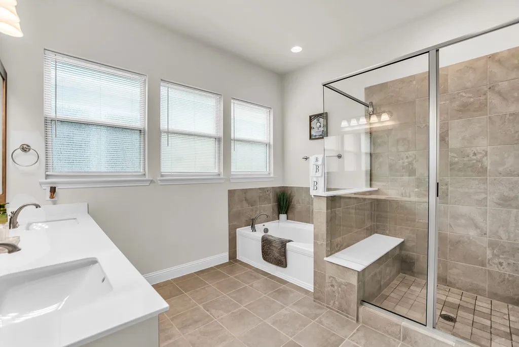 Dual vanity with undermount sinks, white countertop, white soaking tub, glass-enclosed shower, and tiled shower bench