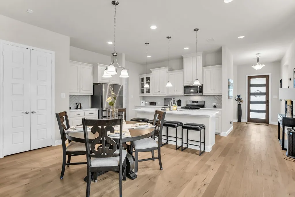 Open-concept kitchen and dining area featuring light wood-finish flooring, white cabinetry, a kitchen island with seating, stainless steel appliances, and a modern entry door