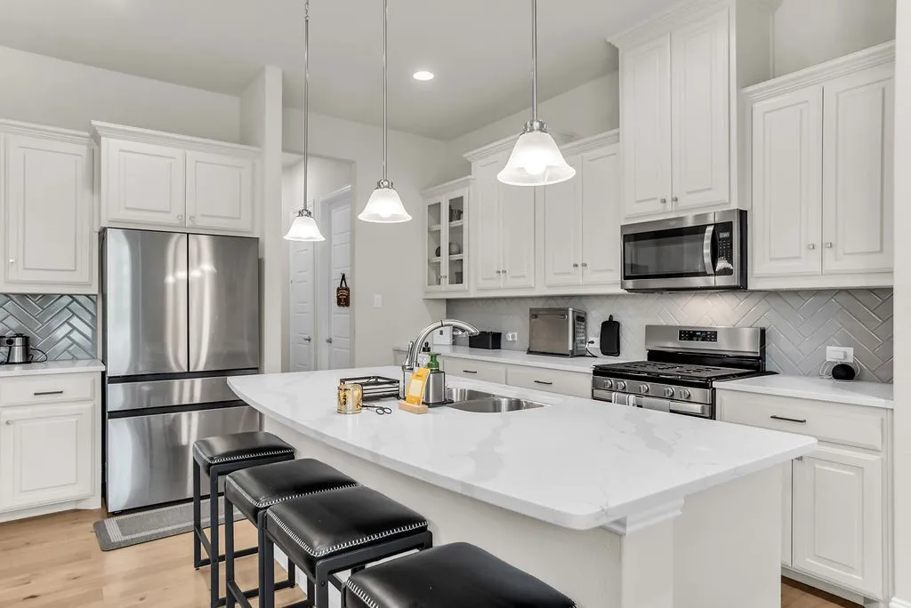 Kitchen featuring white cabinetry, stainless steel appliances, a center island with a sink, white countertops, and wood-finish flooring