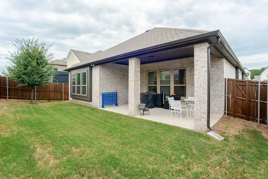 Expansive backyard featuring a covered patio, brick exterior, bay window, and wood privacy fencing