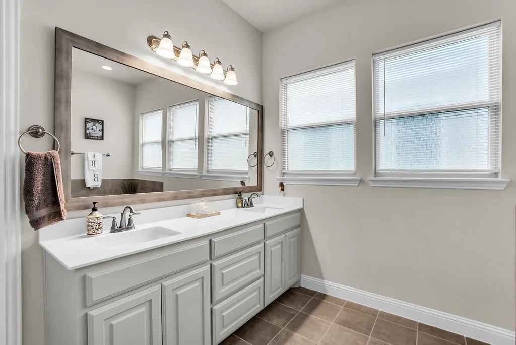 Dual vanity with white countertops, light gray cabinetry, and two windows