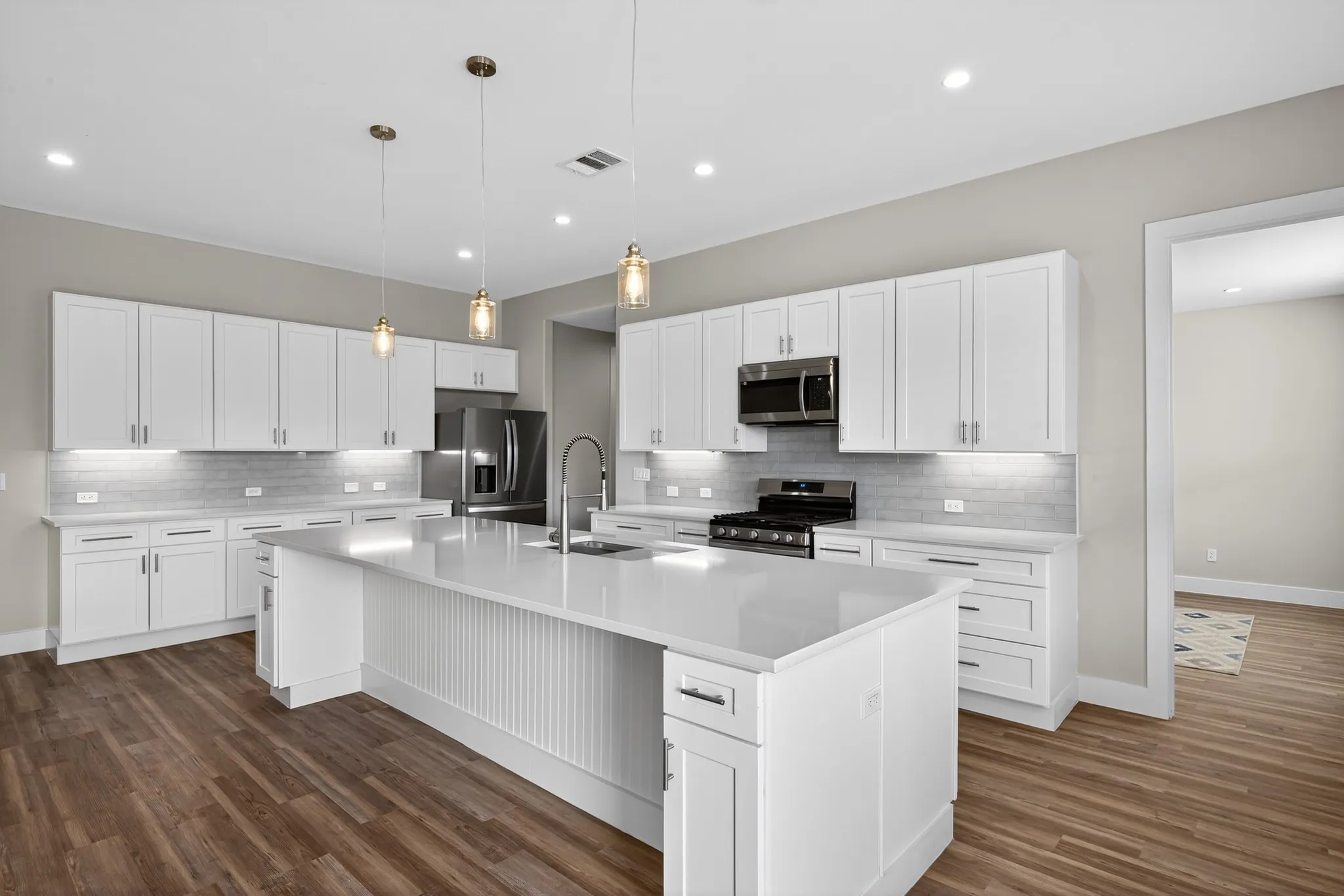 Modern kitchen featuring white cabinetry, stainless steel appliances, a large center island, pendant lighting, and wood-finish flooring