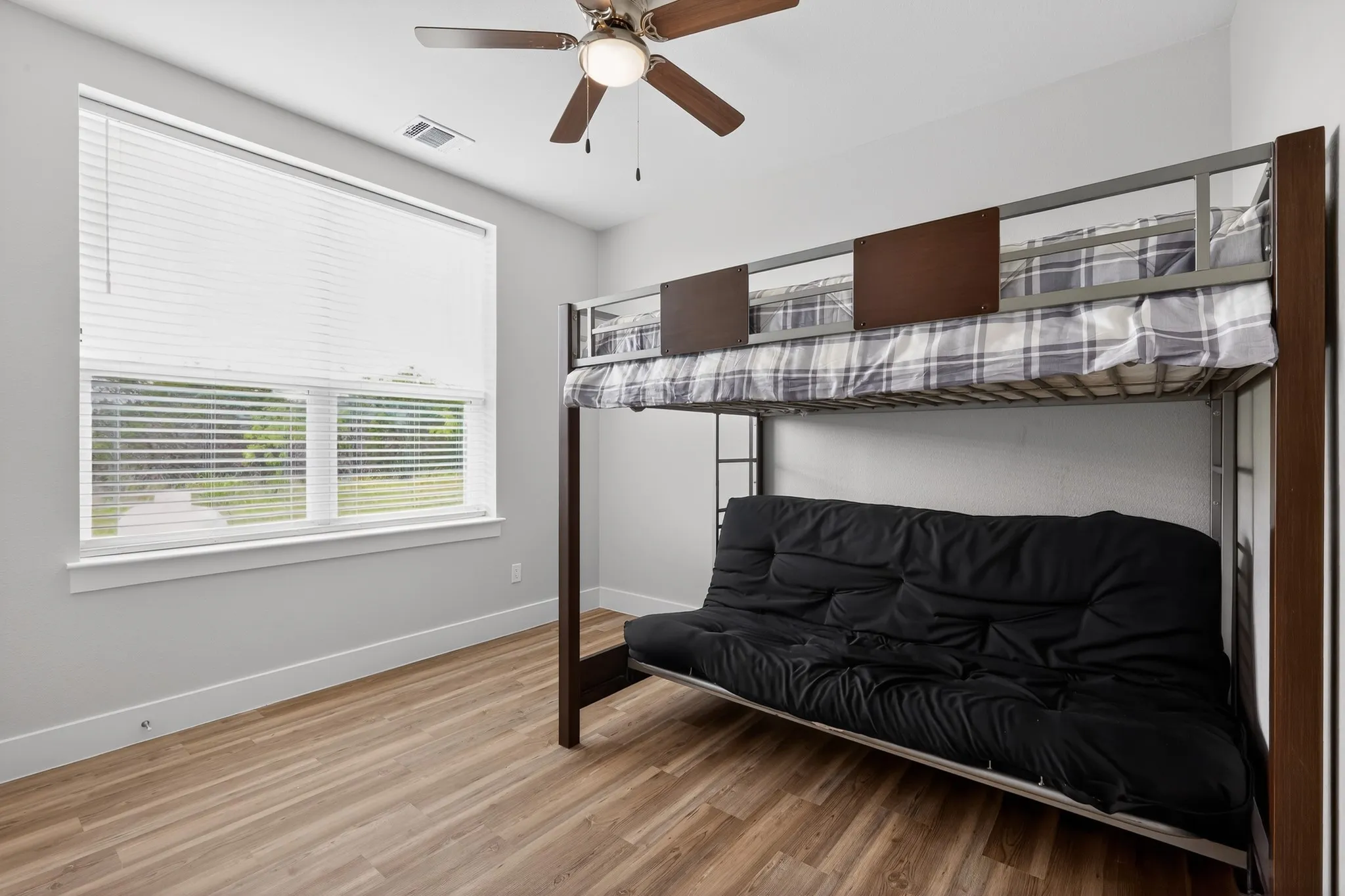 Wood-finish flooring with white trim, large window with blinds, and a ceiling fan with light