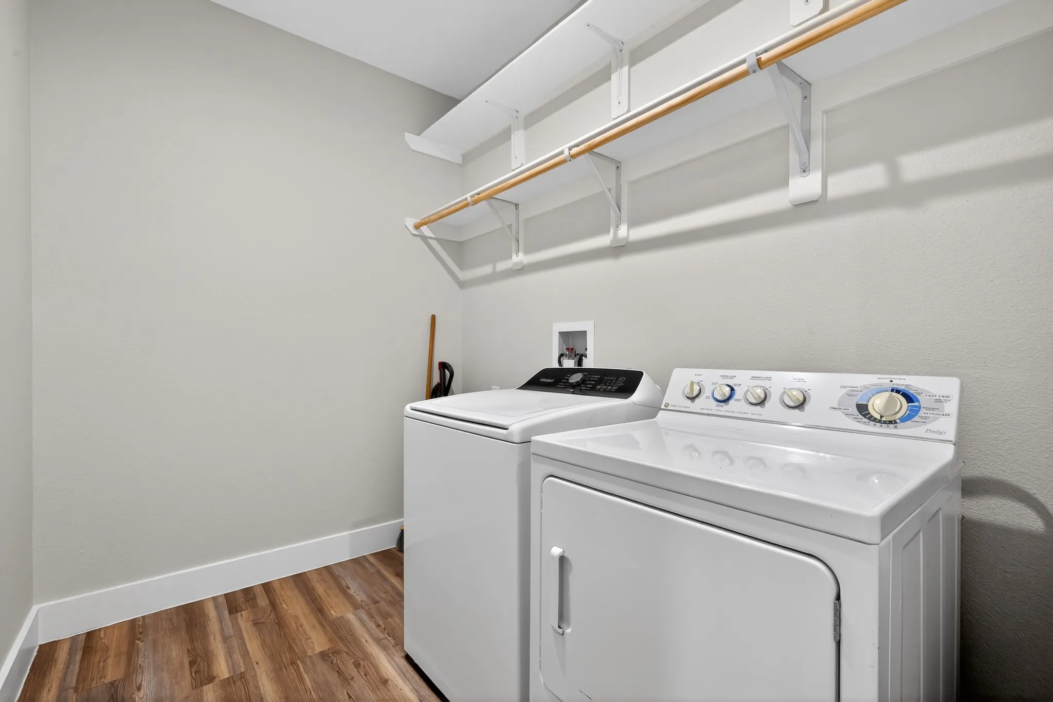 Laundry area featuring wood-finish flooring, light gray walls, and white shelving with a hanging rod