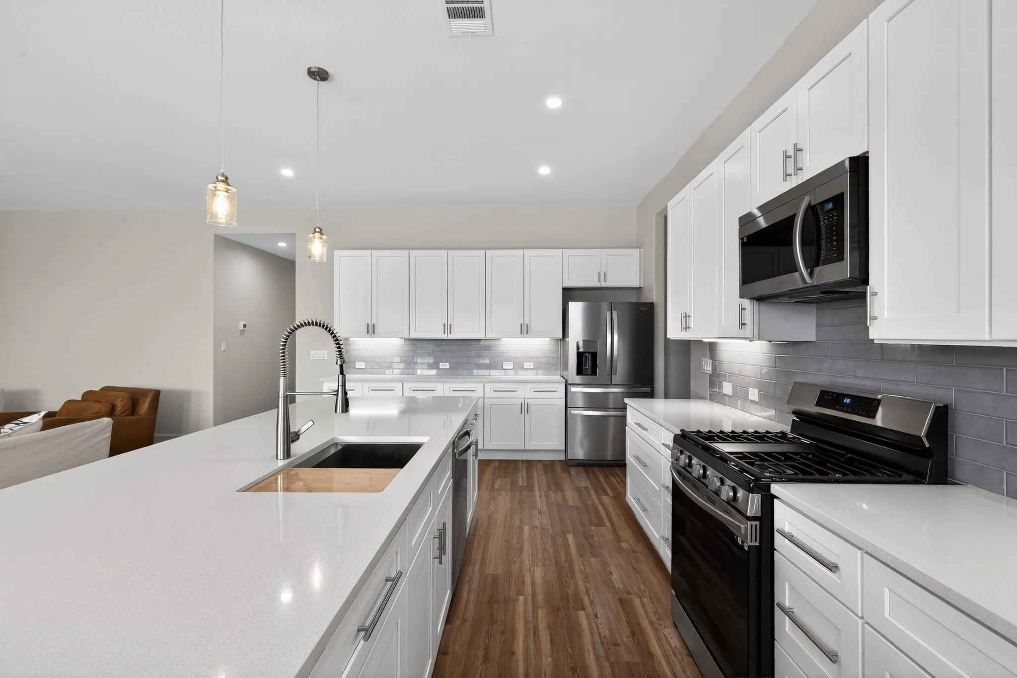 Kitchen featuring a center island with sink, white shaker cabinetry, stainless steel appliances, wood-finish flooring, and subway tile backsplash