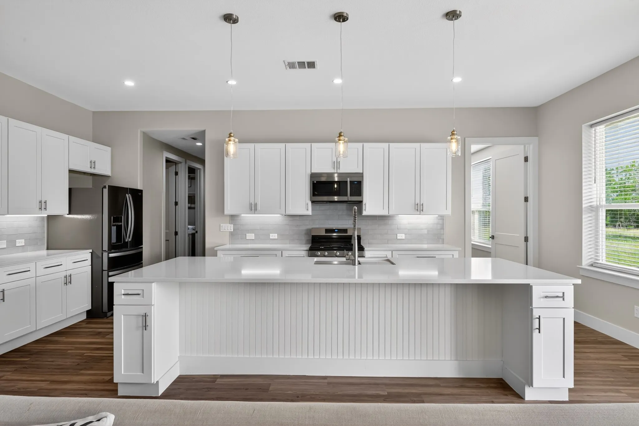 Kitchen with white cabinetry, stainless steel appliances, a center island with pendant lighting, stone countertops, and wood-finish flooring