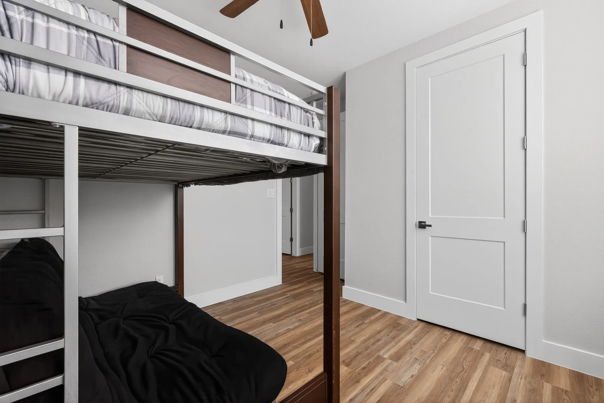 Wood-finish flooring, white trim, and a white two-panel door with matte black hardware
