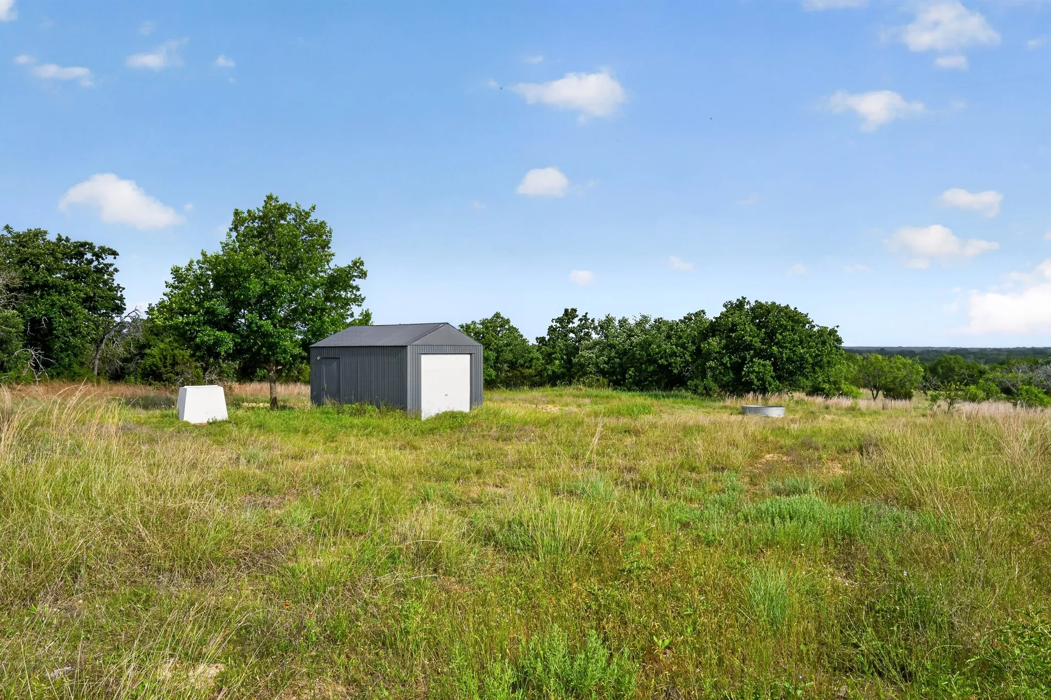 Detached storage shed with a roll-up door, surrounded by mature trees and natural terrain