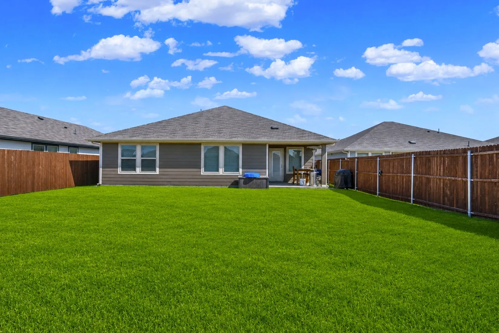 Clean board-and-batten siding and double window banks define the rear elevation, opening out across a deep lawn. The fully enclosed perimeter offers complete privacy from neighboring lots. *Digitally enhanced*