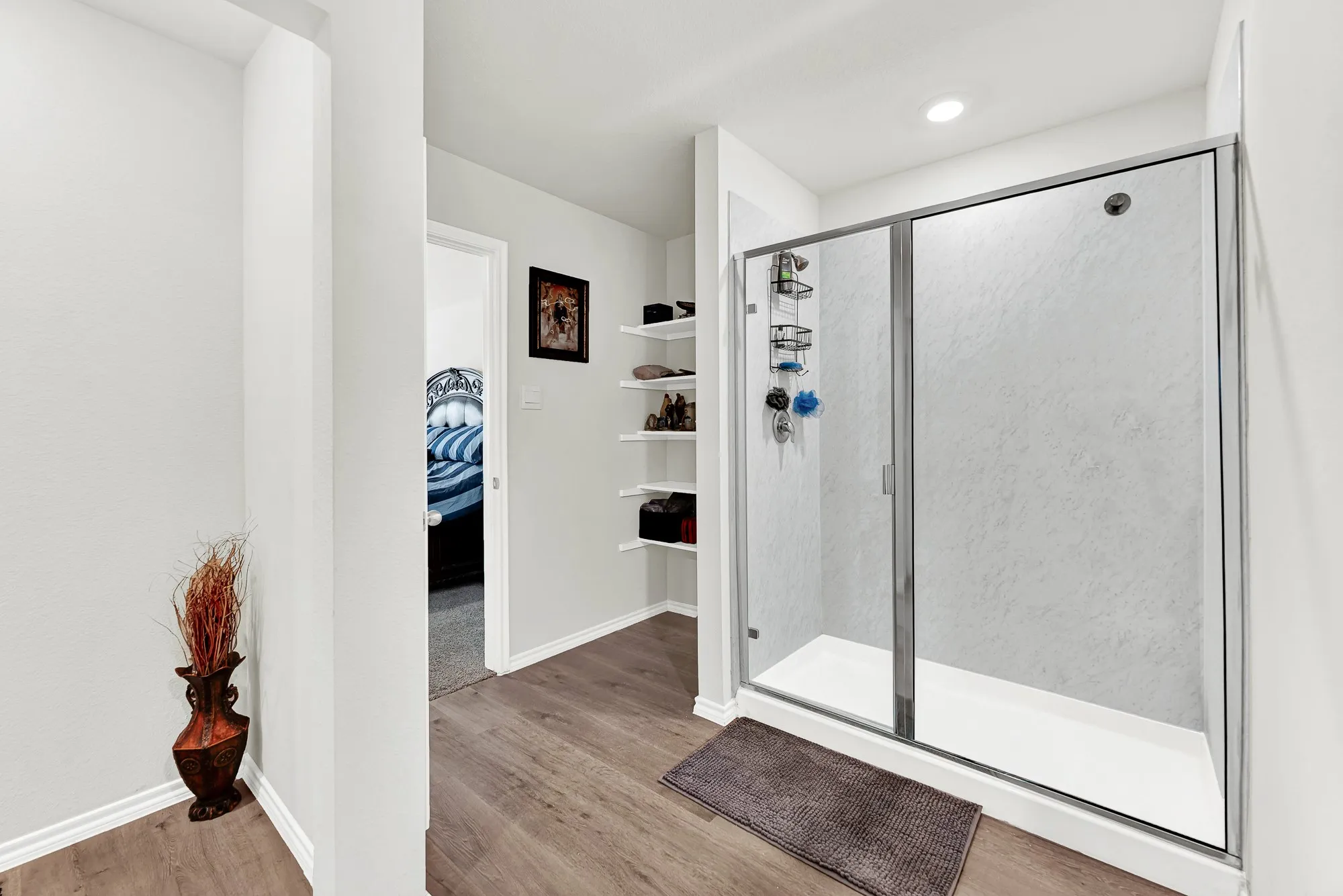 Low-maintenance wood-look flooring extends through the ensuite, highlighting a glass-enclosed shower stall alongside built-in linen shelving. Having plenty of organized storage makes keeping your daily personal essentials neat and simple.