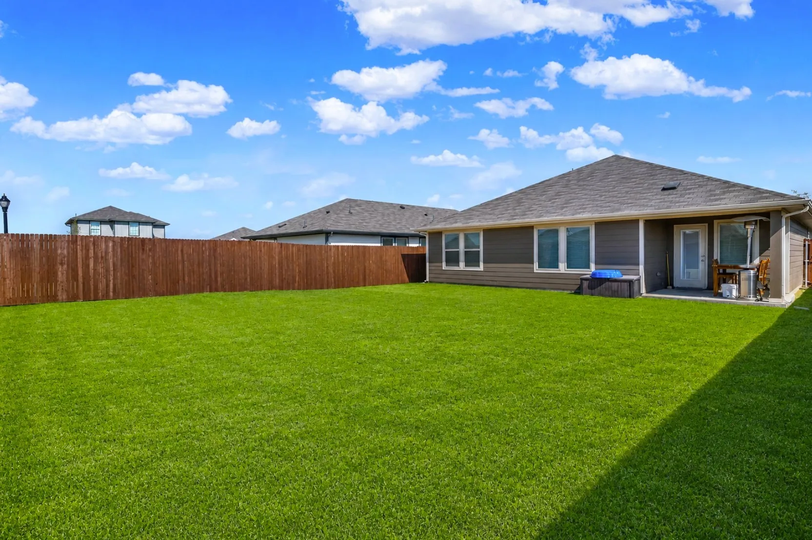 This generous yard layout highlights the covered back patio and main rear roofline set against open blue skies. It creates an ideal outdoor space for weekend barbecues and relaxed outdoor dining. *Digitally Enhanced*