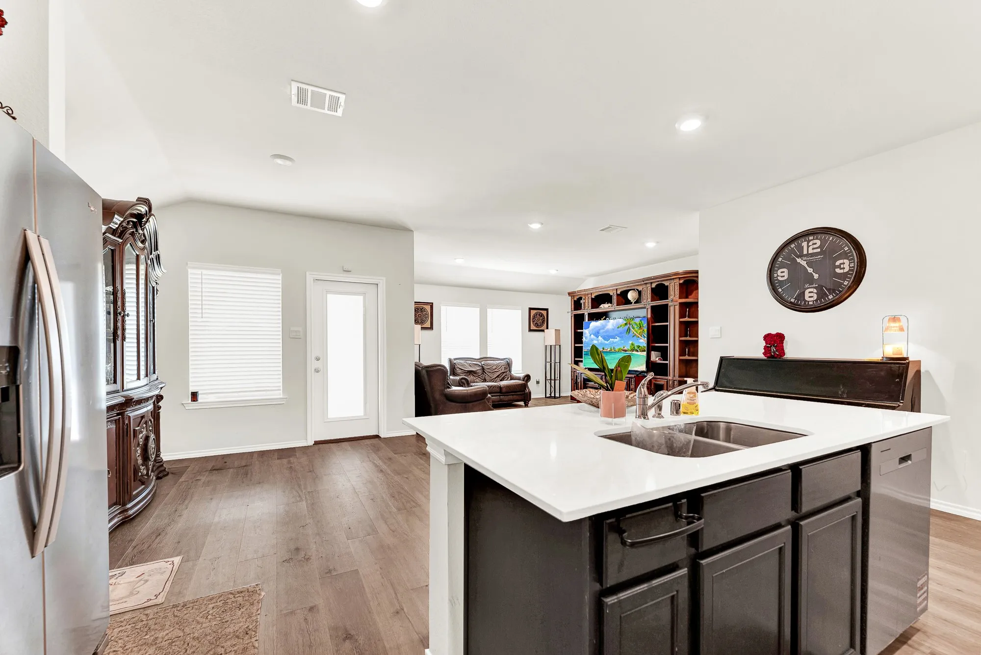 The functional island holds a dual-basin sink and opens directly to the adjacent living area and sunny patio entrance. Chatting with guests while preparing drinks makes everyday entertaining feel relaxed and natural.