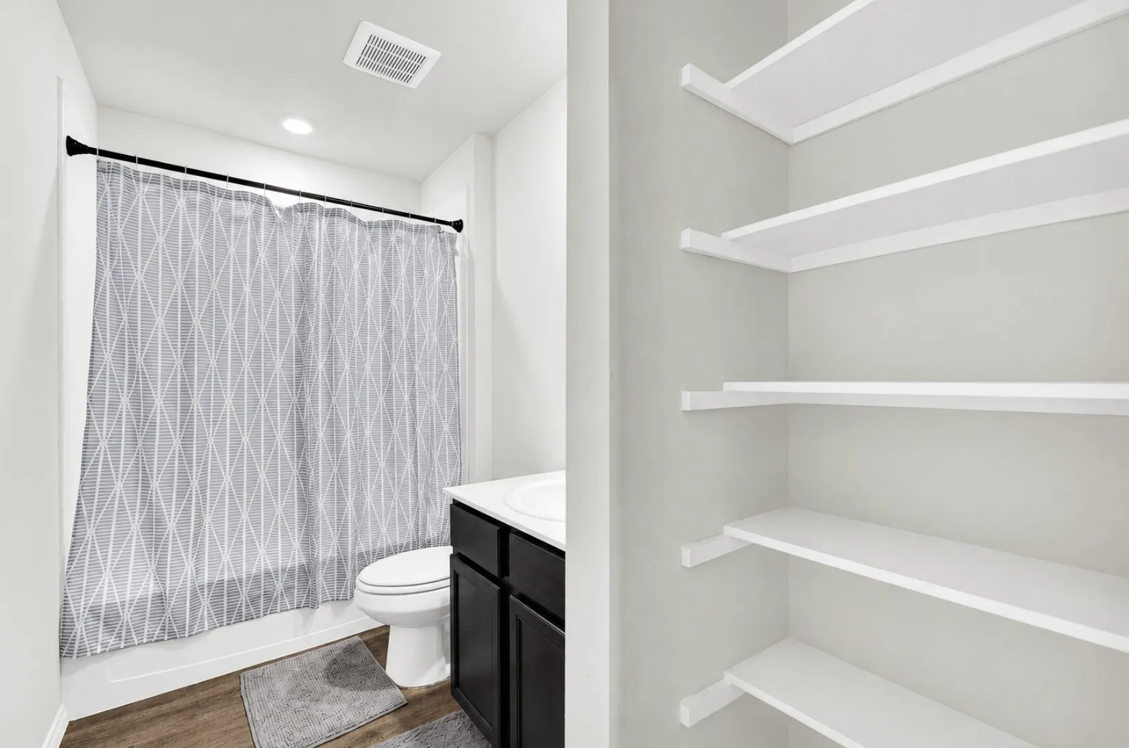 The full guest bathroom includes a dark vanity cabinet, a tub and shower combination, and built-in open linen shelving for extra towel storage. Having a well-appointed full bath nearby keeps routines running smoothly for family and visitors alike.