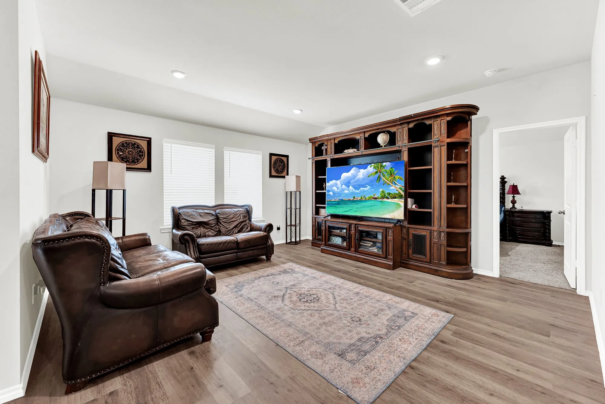 Continuous wood-look flooring and soft wall tones anchor this inviting main living area, highlighted by double windows and recessed lighting overhead. It offers a warm setting where you can kick back for family movie nights or catch the big game with friends.
