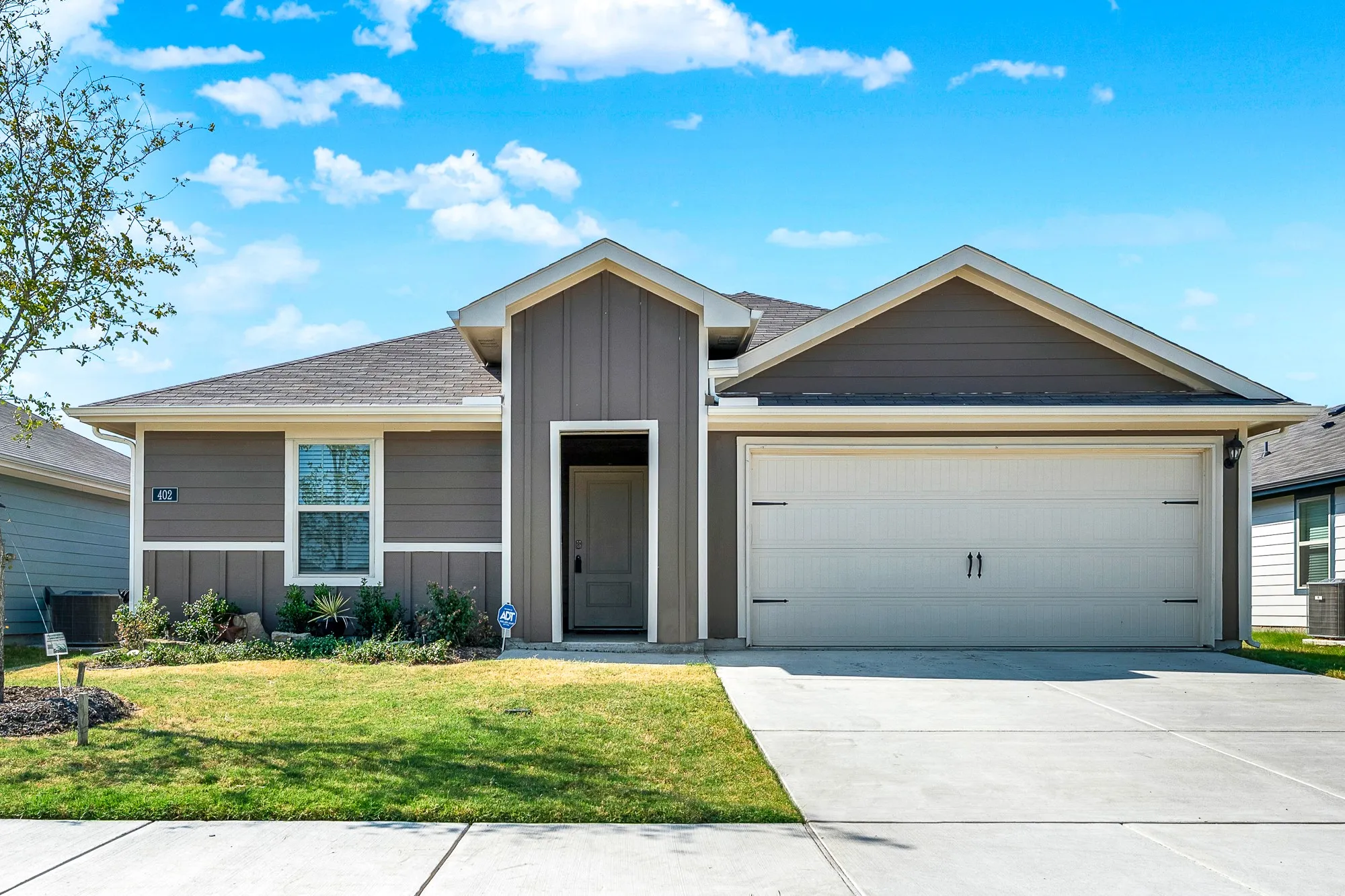 Featuring crisp board-and-batten accent siding, clean gabled rooflines, and a spacious two-car garage, this modern single-story elevation delivers excellent curb appeal. Crisp landscaping beds and a concrete driveway create a welcoming entrance to the home.