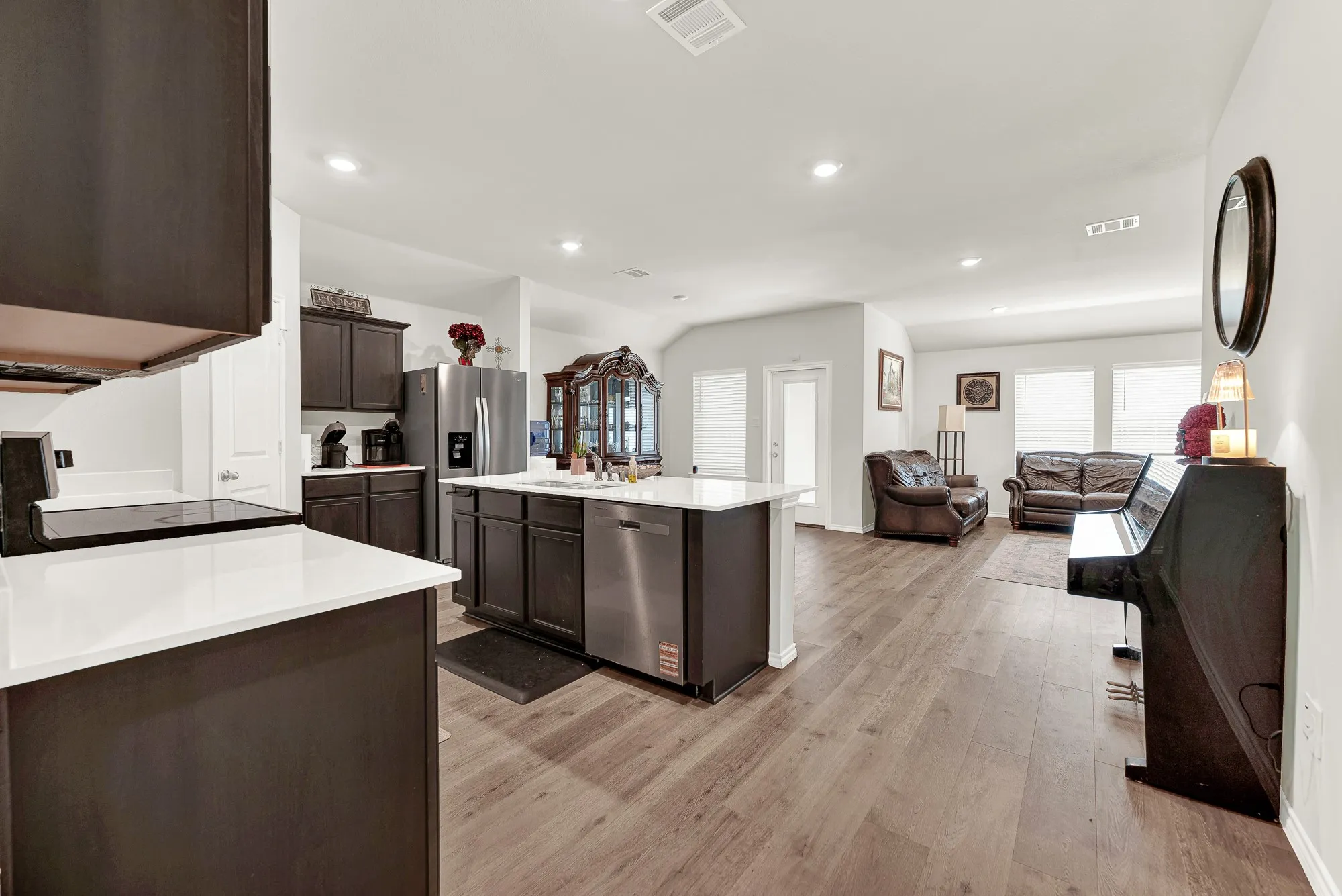 Looking from the hallway entry, this panoramic perspective captures the seamless flow between the kitchen, central dining space, and main living room. Smooth wood-look flooring and soft recessed lighting pull the entire heart of the home together into one bright, inviting space