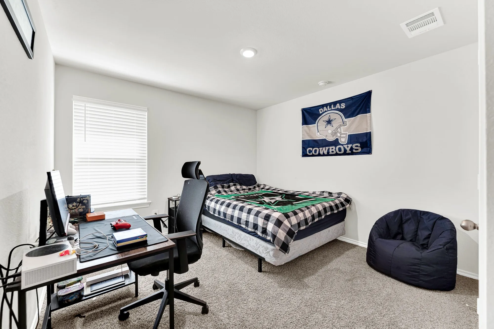 Neutral carpeting and soft walls frame this cozy secondary bedroom, filled with natural light from a large single window. It offers a comfortable personal haven for family members or visiting guests.