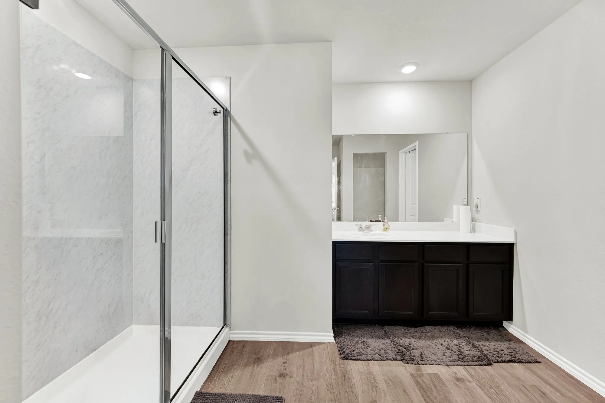 The primary bathroom features a dark vanity cabinet with white counter space, a large wall-to-wall mirror, and a sleek walk-in shower with a framed glass door. It feels like your own private spa where you can easily prep for the day ahead.
