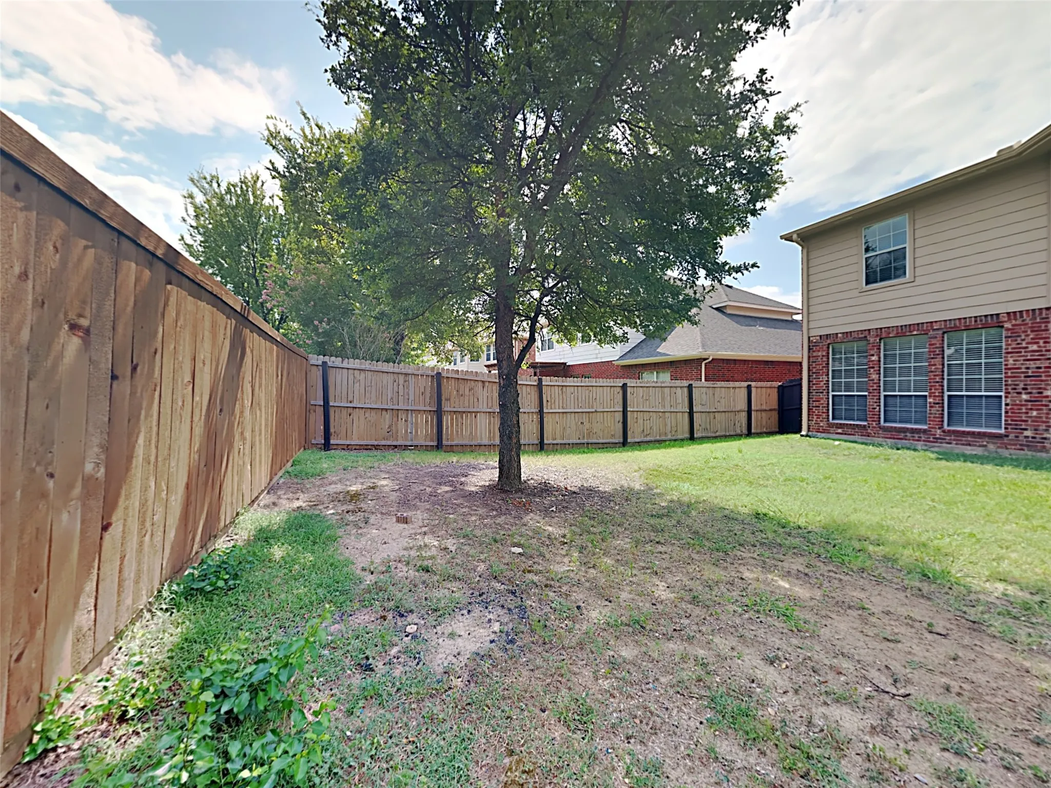 Expansive backyard featuring a mature tree, wood privacy fencing, and a combination brick and siding exterior