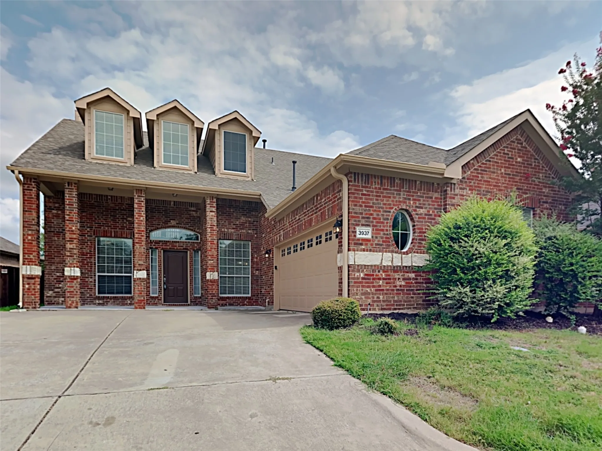 Red brick facade with a two-car garage, concrete driveway, and dormer windows