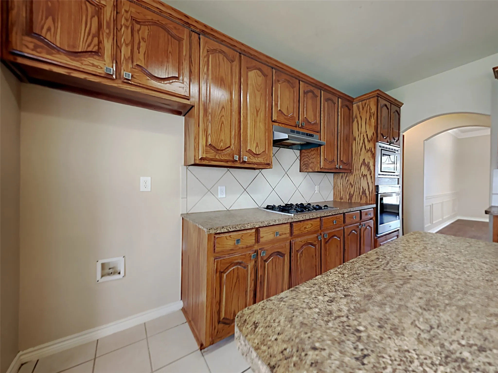 Kitchen featuring wood cabinetry, a built-in oven, granite-style countertops, a gas cooktop, and tile flooring