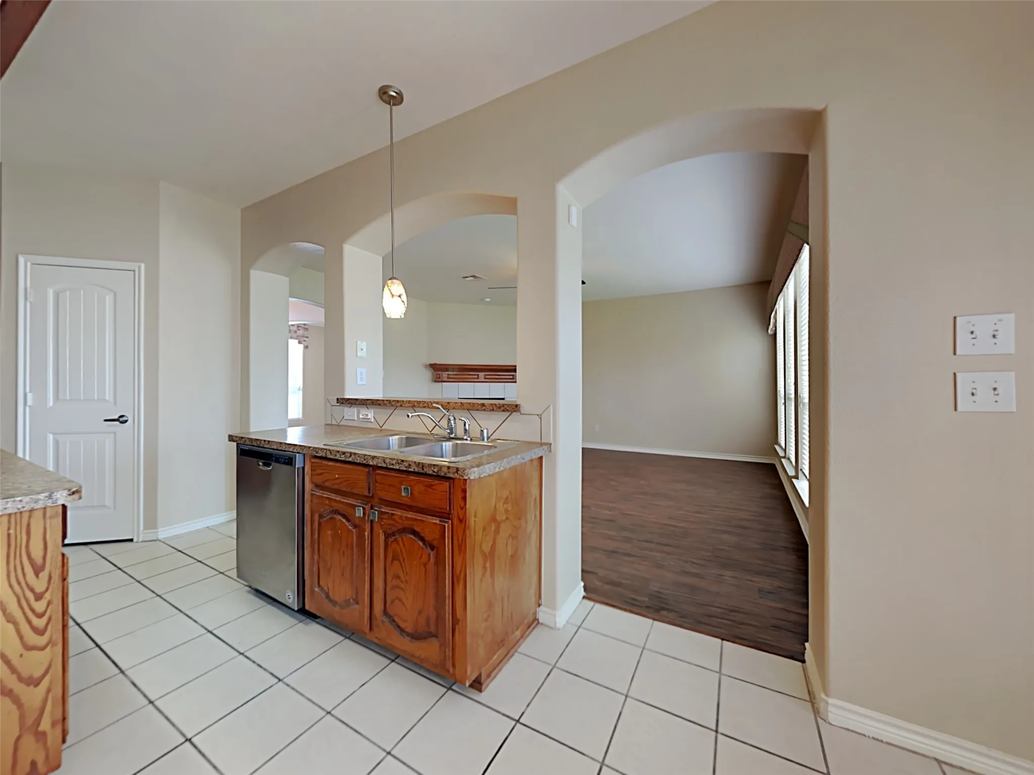 Kitchen featuring tile flooring, wood cabinetry, stone countertops, and a stainless steel dishwasher
