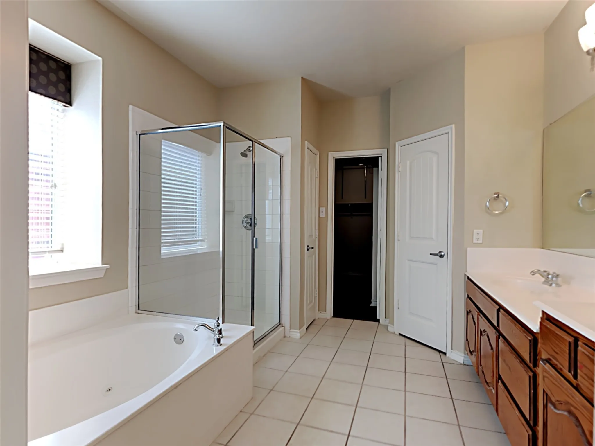 Tiled flooring, double vanity with wood-finish cabinetry, built-in soaking tub, glass-enclosed shower, and a private water closet