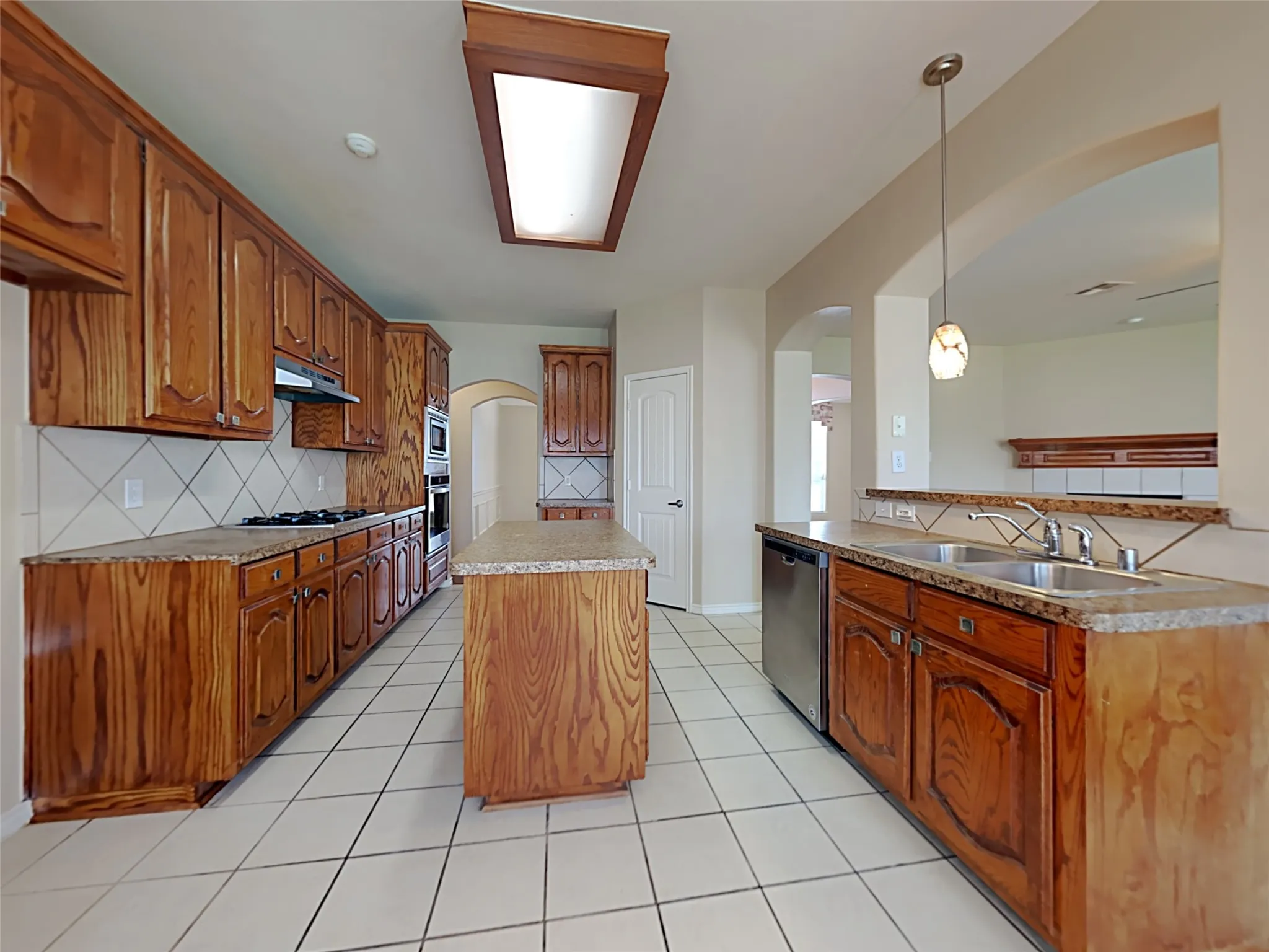 Kitchen featuring wood-finish cabinetry, light-toned countertops, a center island, and stainless steel appliances