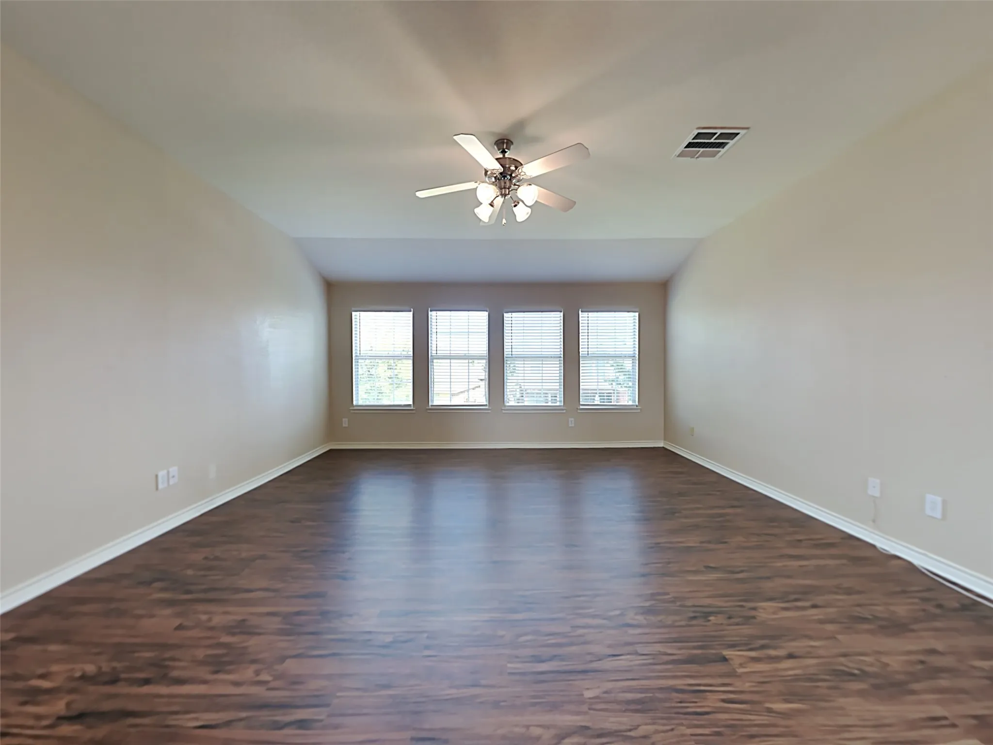 Vaulted ceilings, wood-finish flooring, multiple windows with blinds, and a ceiling fan with integrated lighting
