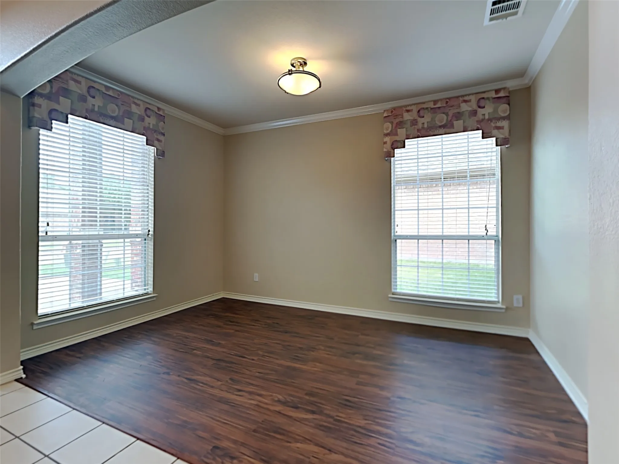 Wood-finish flooring, two large windows with blinds, recessed ceiling light, and crown molding