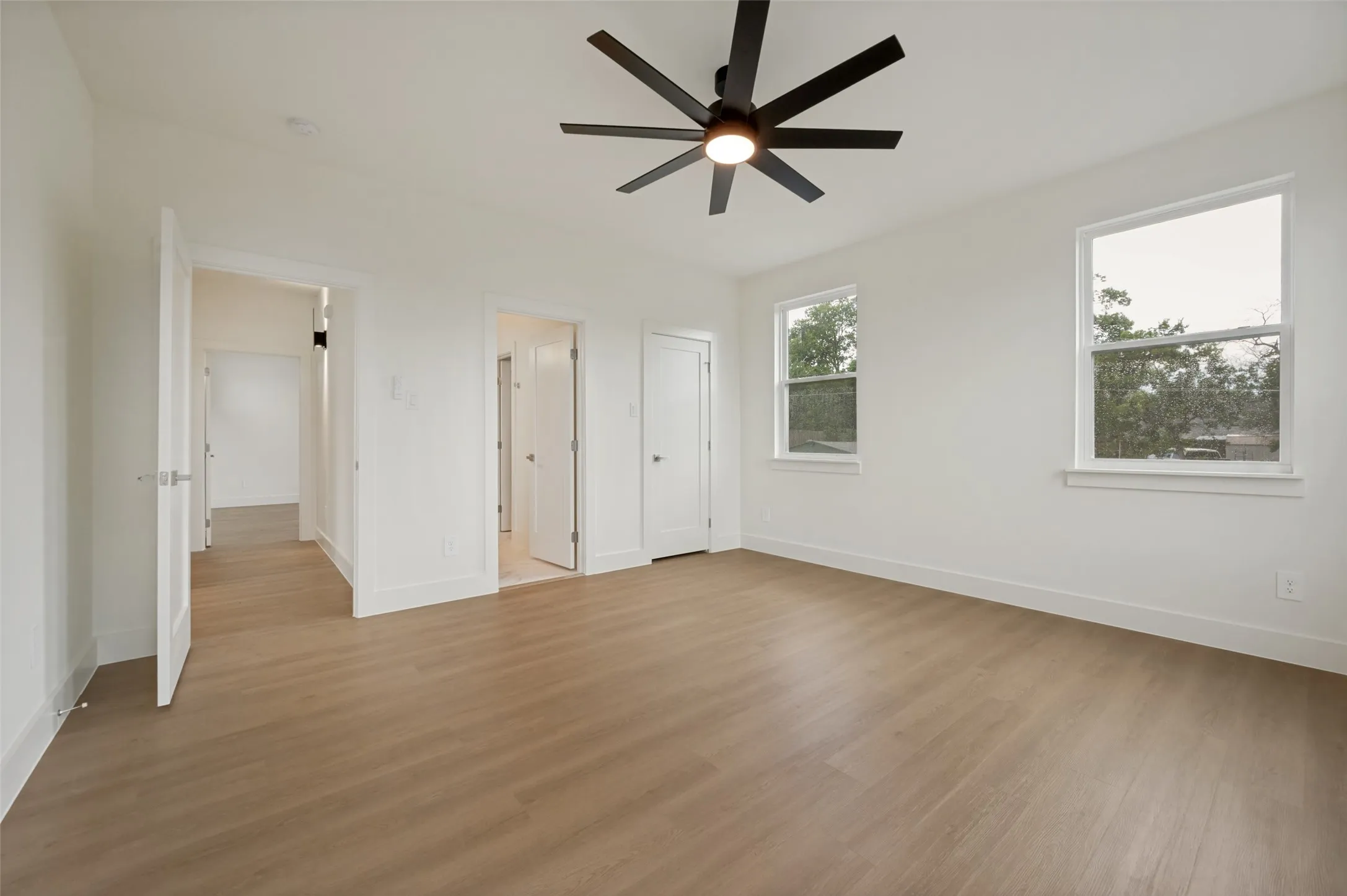 Spacious room with wood-finish flooring, two windows, and a black ceiling fan with integrated lighting