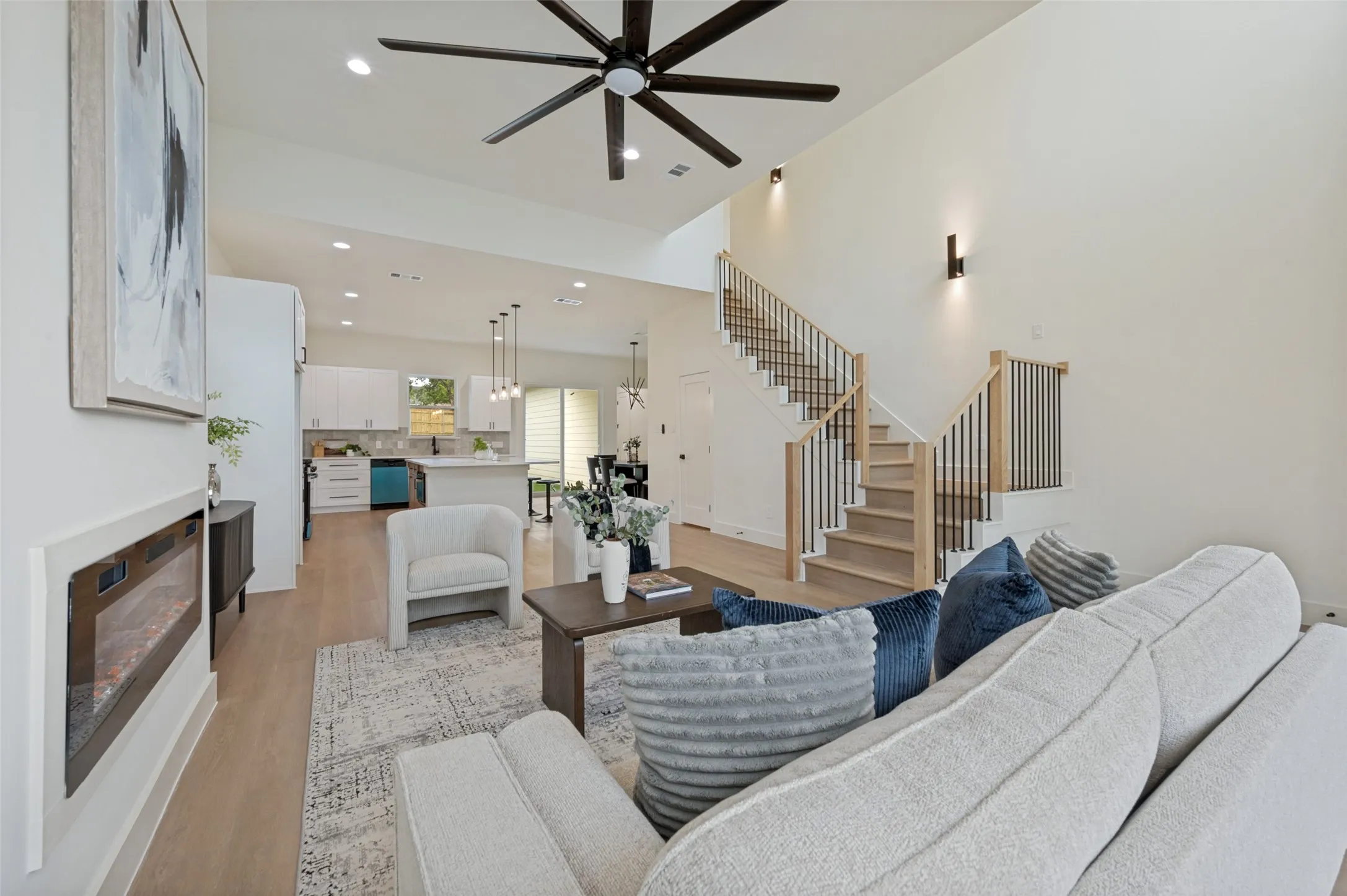 Vaulted ceilings, wood-finish flooring, staircase with metal balusters, built-in electric fireplace, and recessed lighting