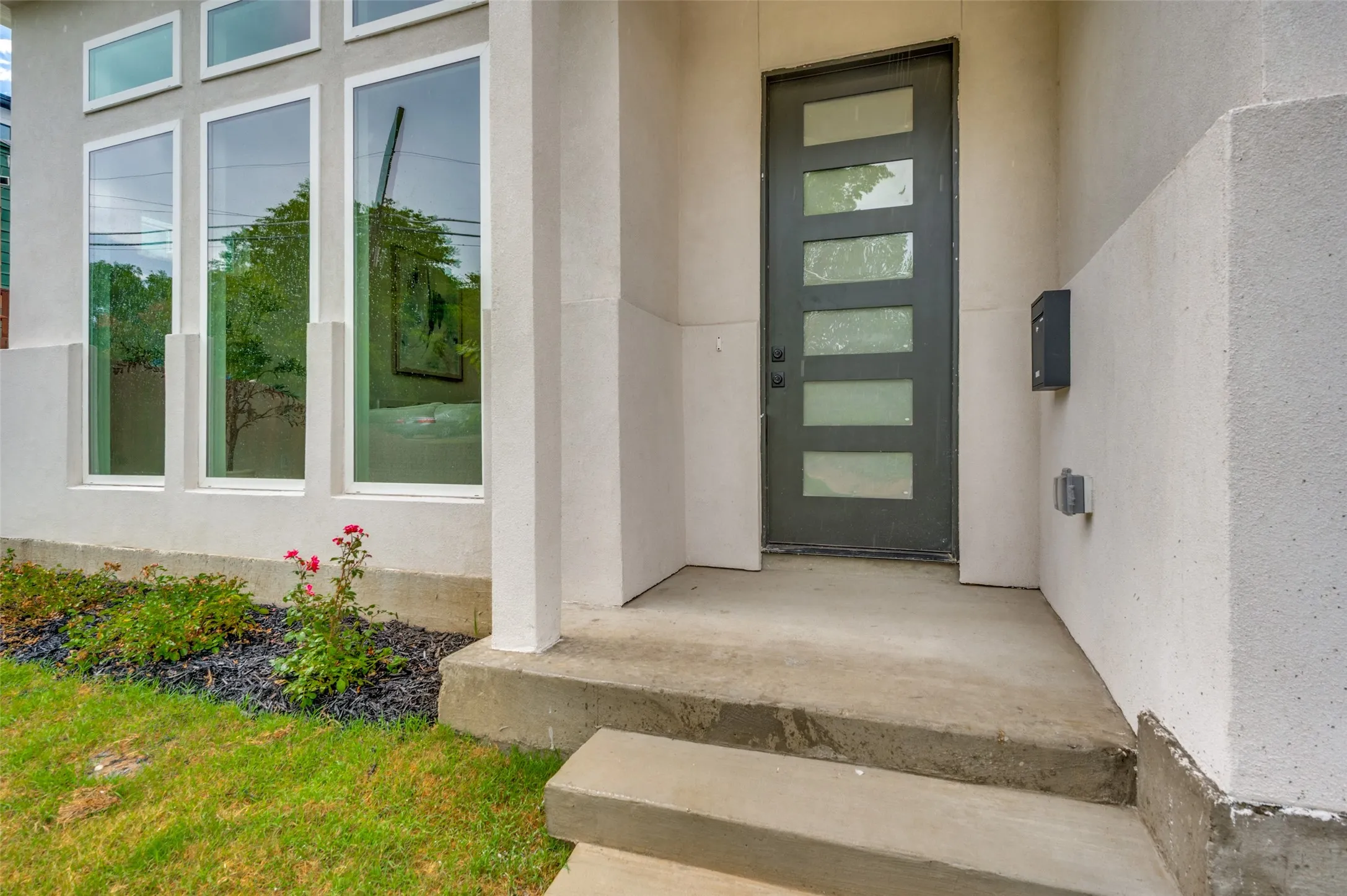 Contemporary exterior with a dark-frame multi-pane entry door, multiple vertical windows, and a concrete entry pad