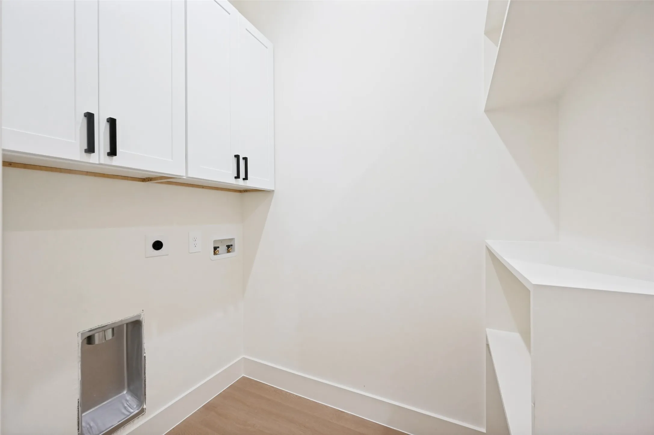 White cabinetry with dark hardware, built-in shelving, wood-finish flooring, and white baseboards
