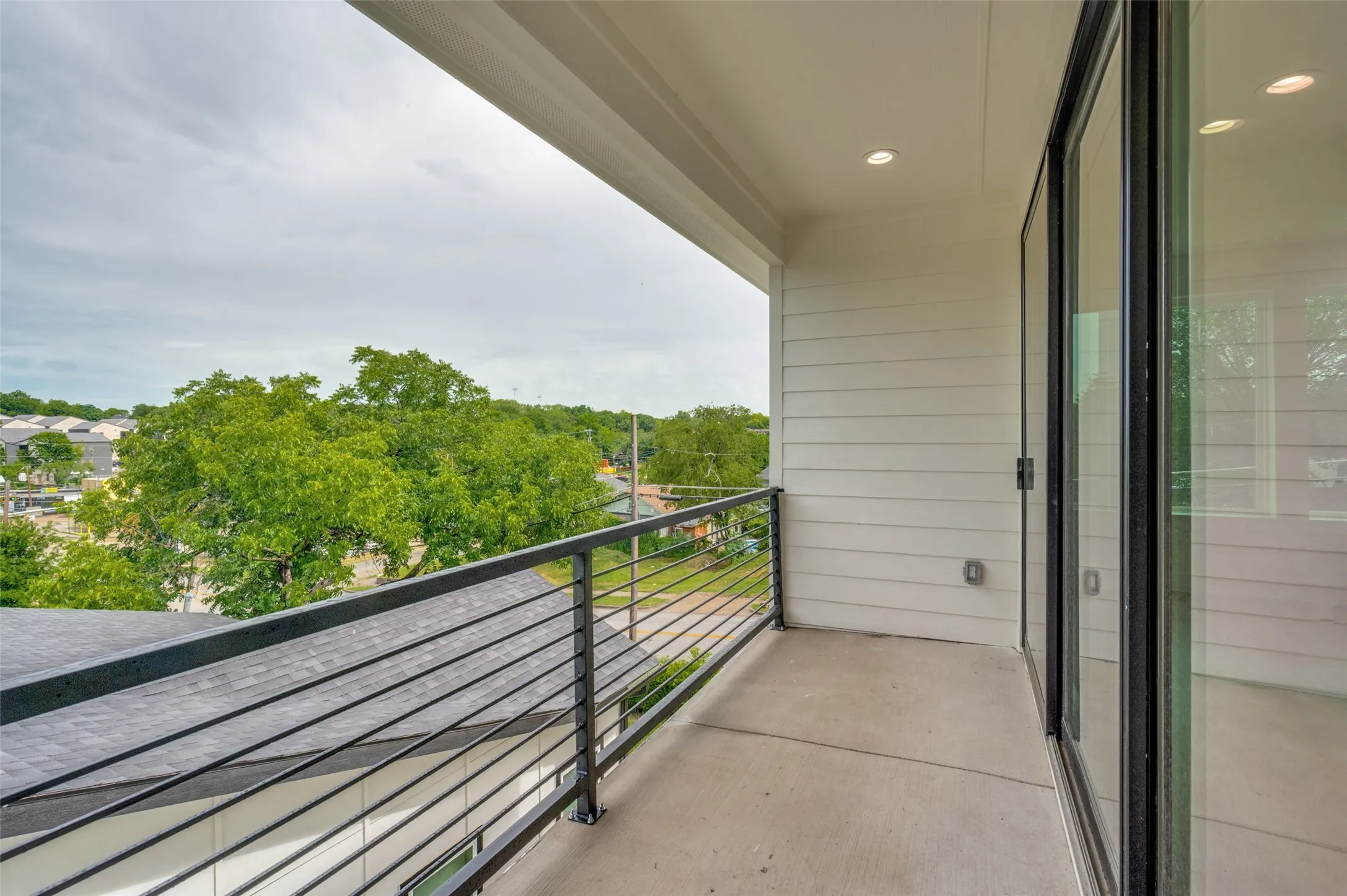 Concrete balcony with a metal railing, recessed lighting, and a sliding glass door