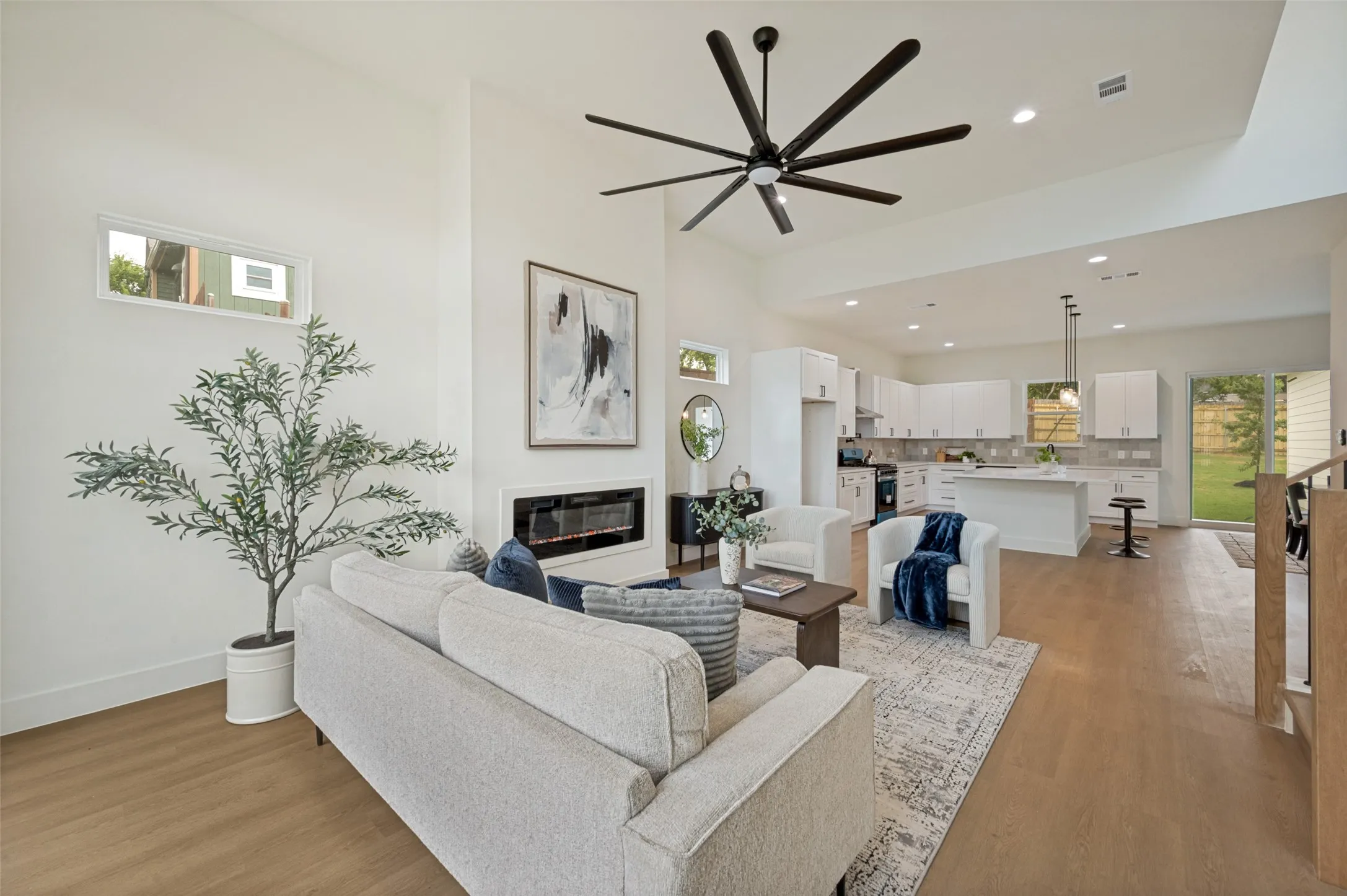 Vaulted ceilings with a ceiling fan, wood-finish flooring, a linear electric fireplace, and a kitchen featuring white cabinetry and an island with bar seating