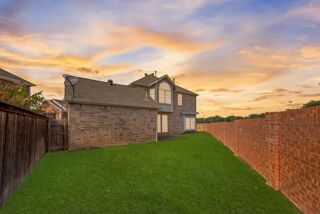 Expansive backyard featuring a manicured lawn, full brick exterior, and a brick privacy wall