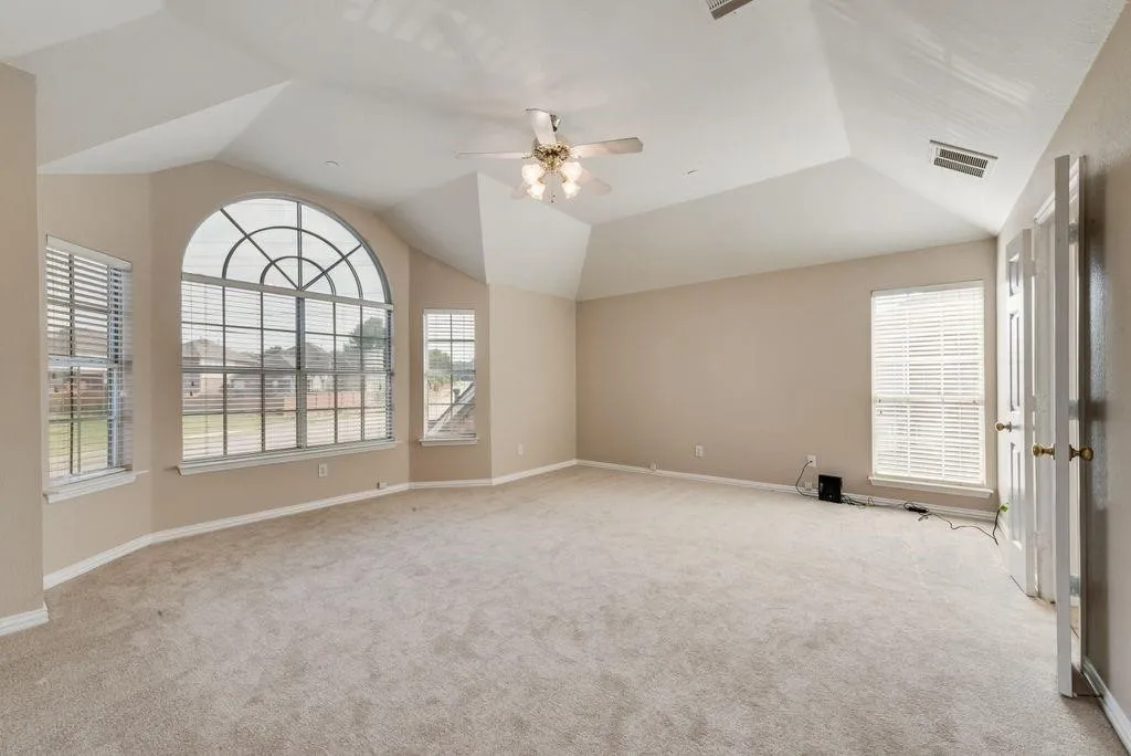 Vaulted ceiling with a ceiling fan, arched transom window, dual windows with blinds, and neutral carpeting